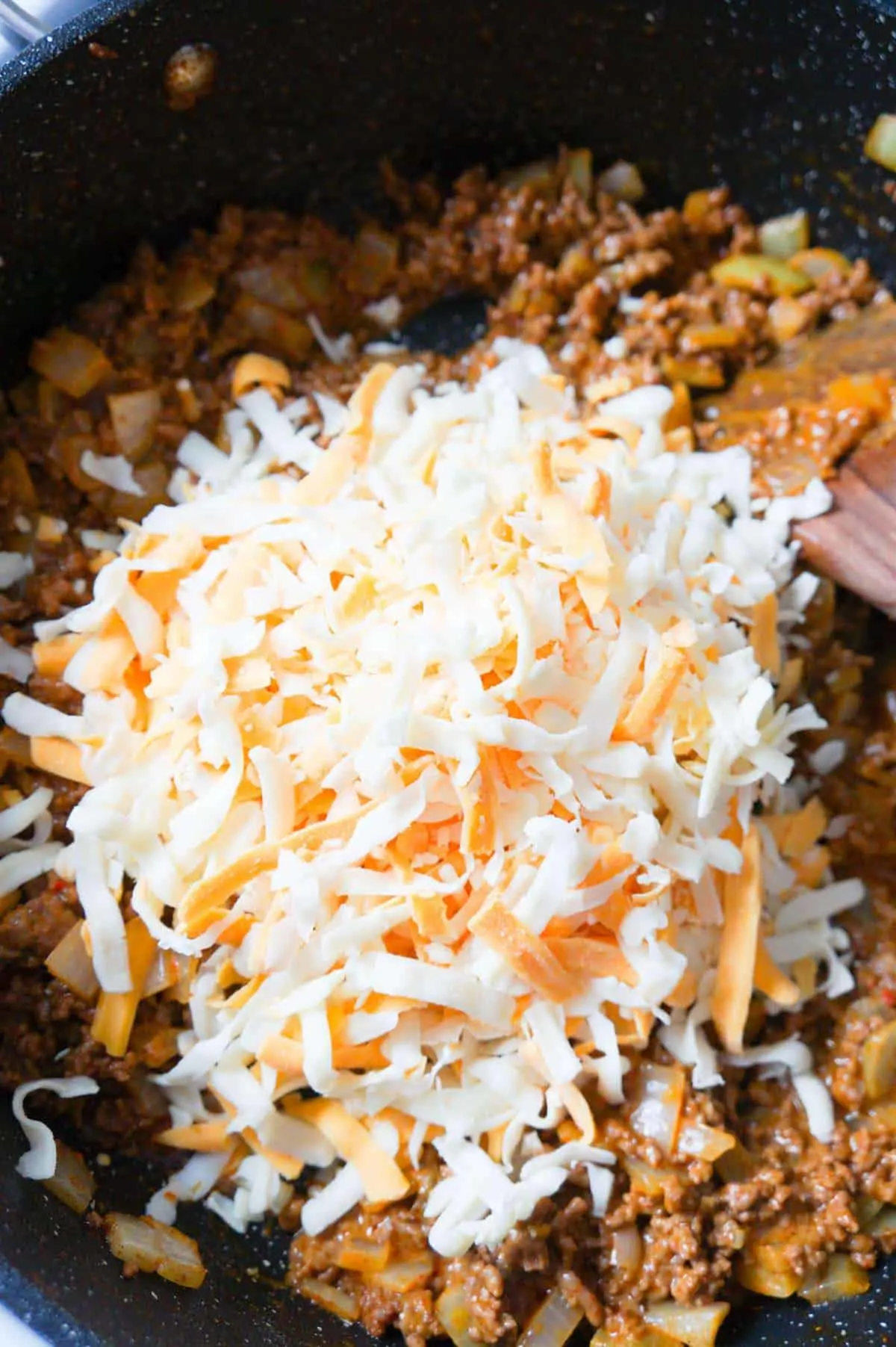 shredded cheese on top of ground beef mixture in a saute pan