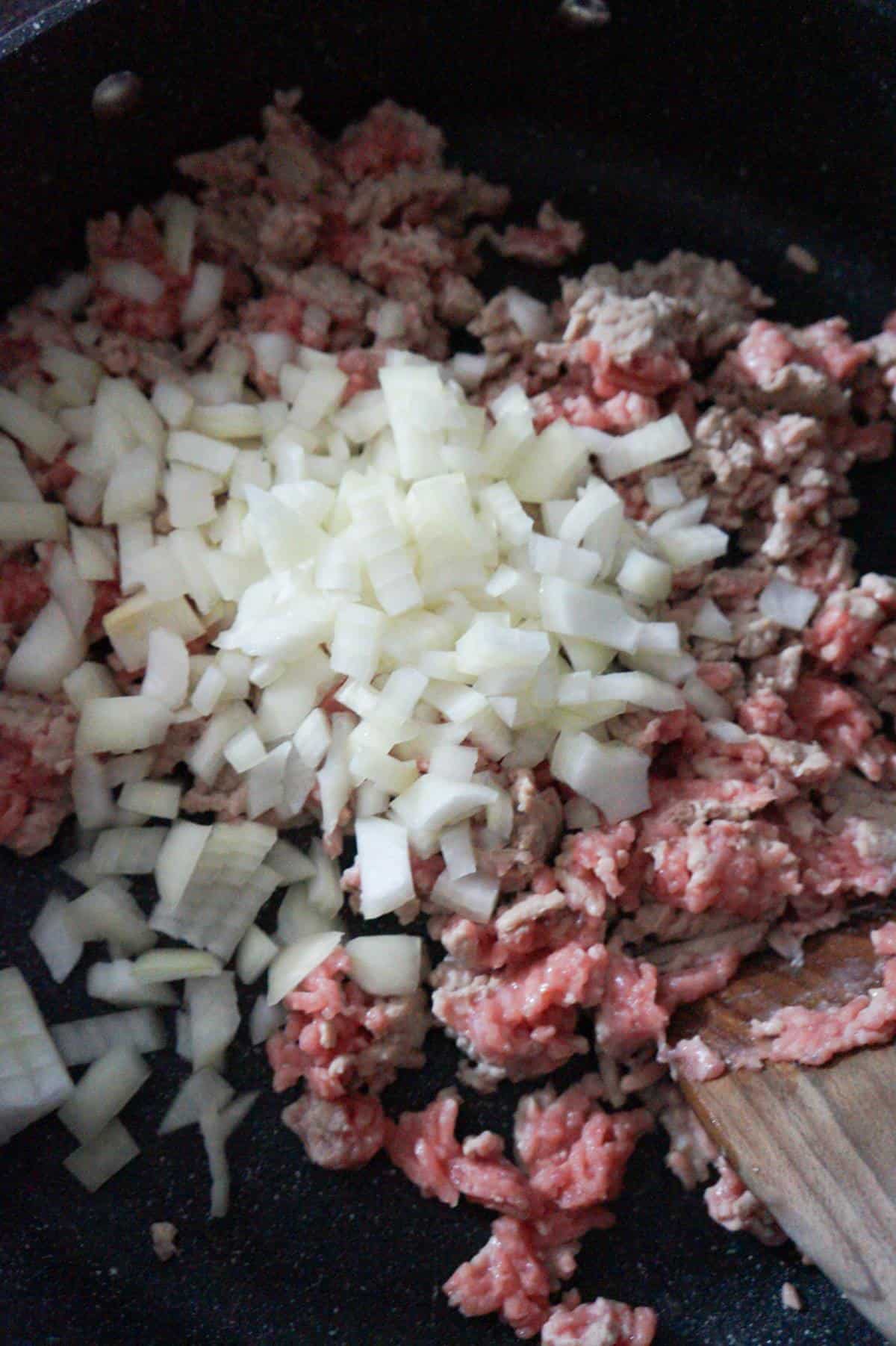 diced onions on top of ground chicken in a saute pan