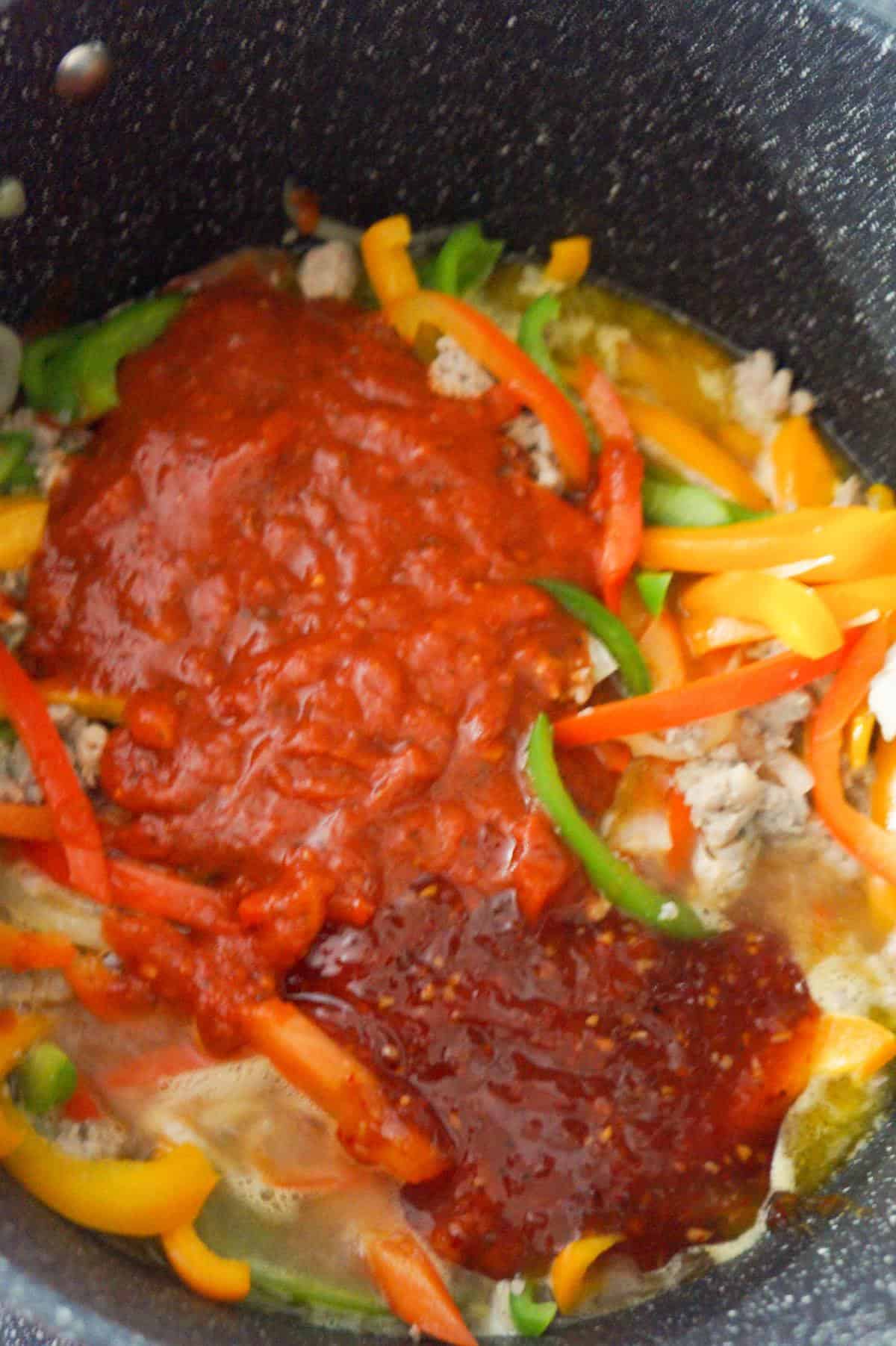 marinara and sweet thai chili sauce on top of sausage and peppers mixture in a large pot