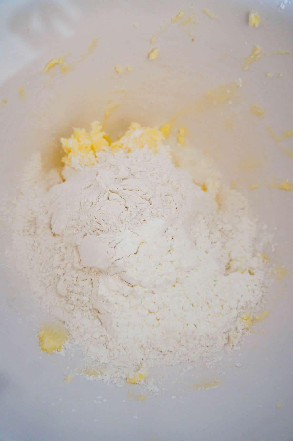 flour and cornstarch on top of butter and icing sugar mixture in a mixing bowl