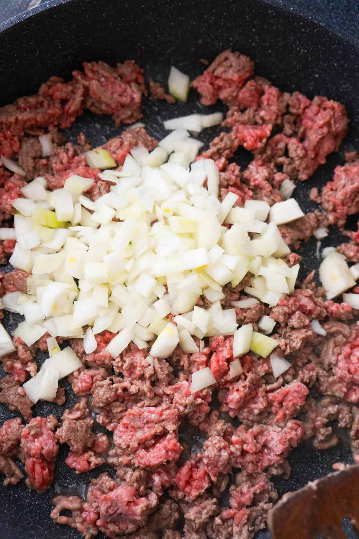 diced onions on top of ground beef in a pan