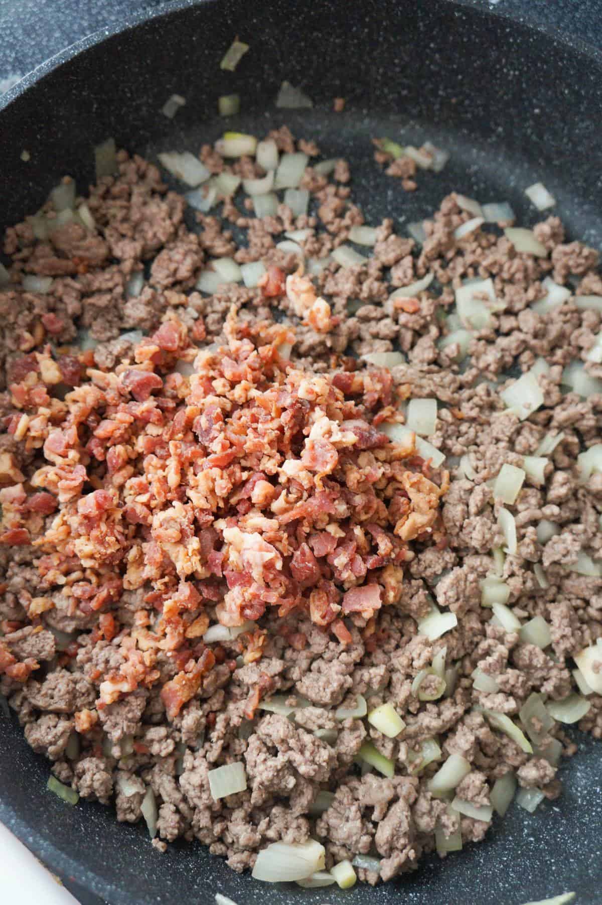 crumbled bacon on top of cooked ground beef and onions in a pan