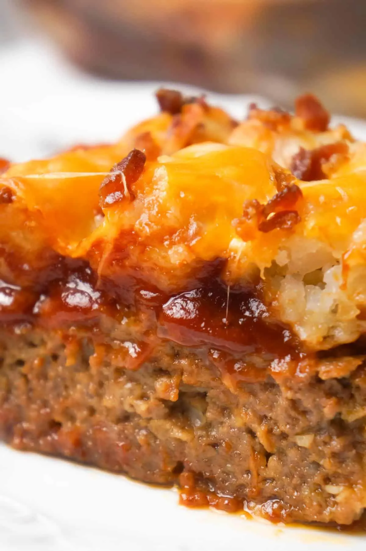 Cheesy Tater Tot Meatloaf Casserole is an easy ground beef dinner recipe with a meatloaf base, topped with a ketchup and bbq sauce glaze, tater tots, shredded cheese and crumbled bacon.