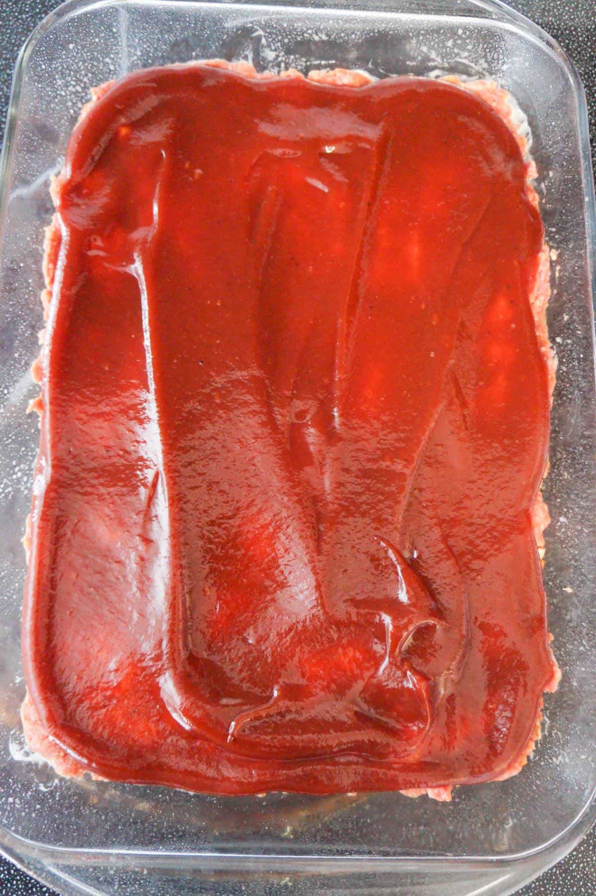 bbq sauce on top of meatloaf mixture in a baking dish