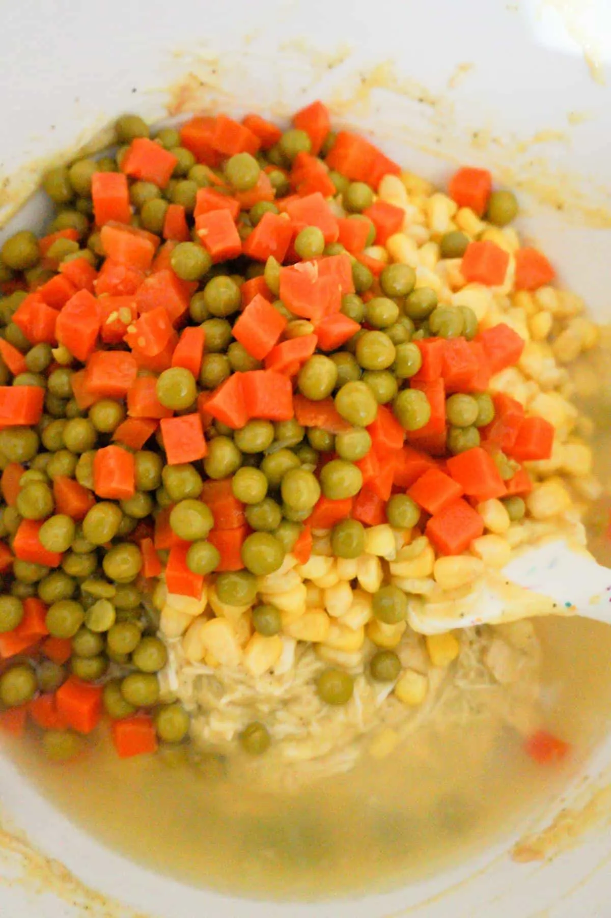peas,carrots and corn on top of chicken in a mixing bowl