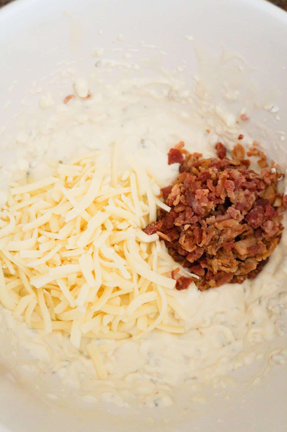 shredded mozzarella and crumbled bacon on top of cream cheese mixture in a mixing bowl