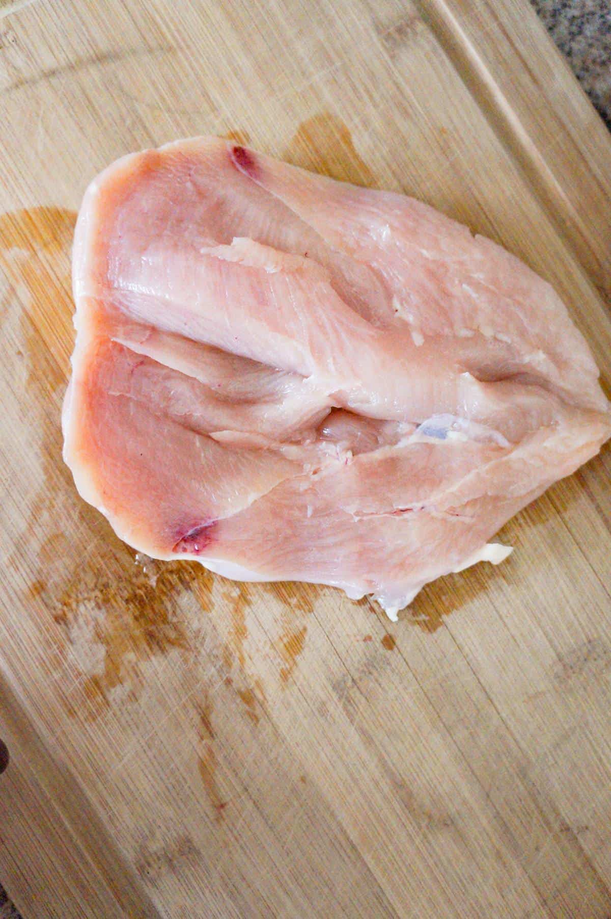 raw chicken breast sliced open on a cutting board