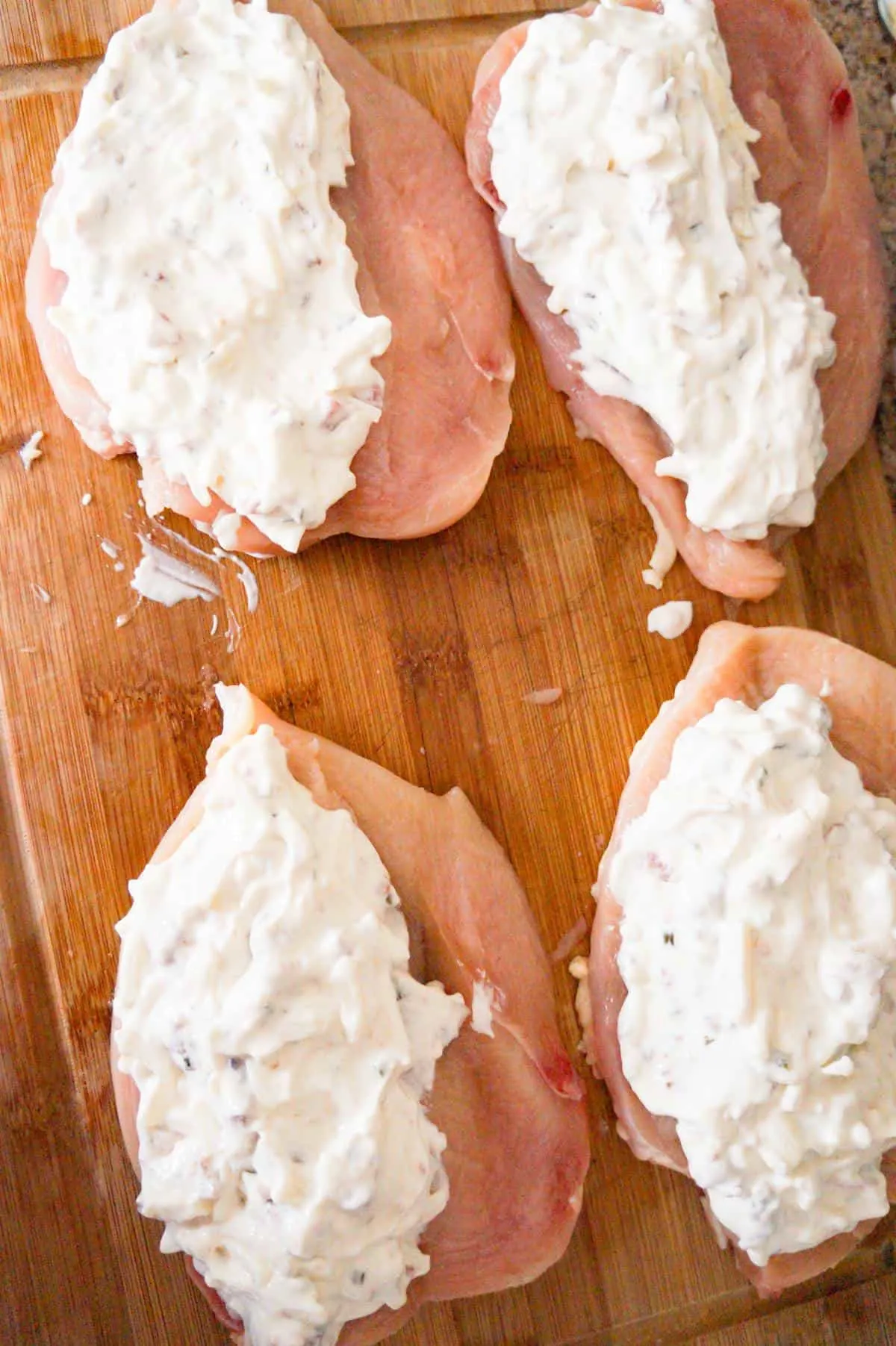 cream cheese mixture on top of raw chicken breasts on a cutting board