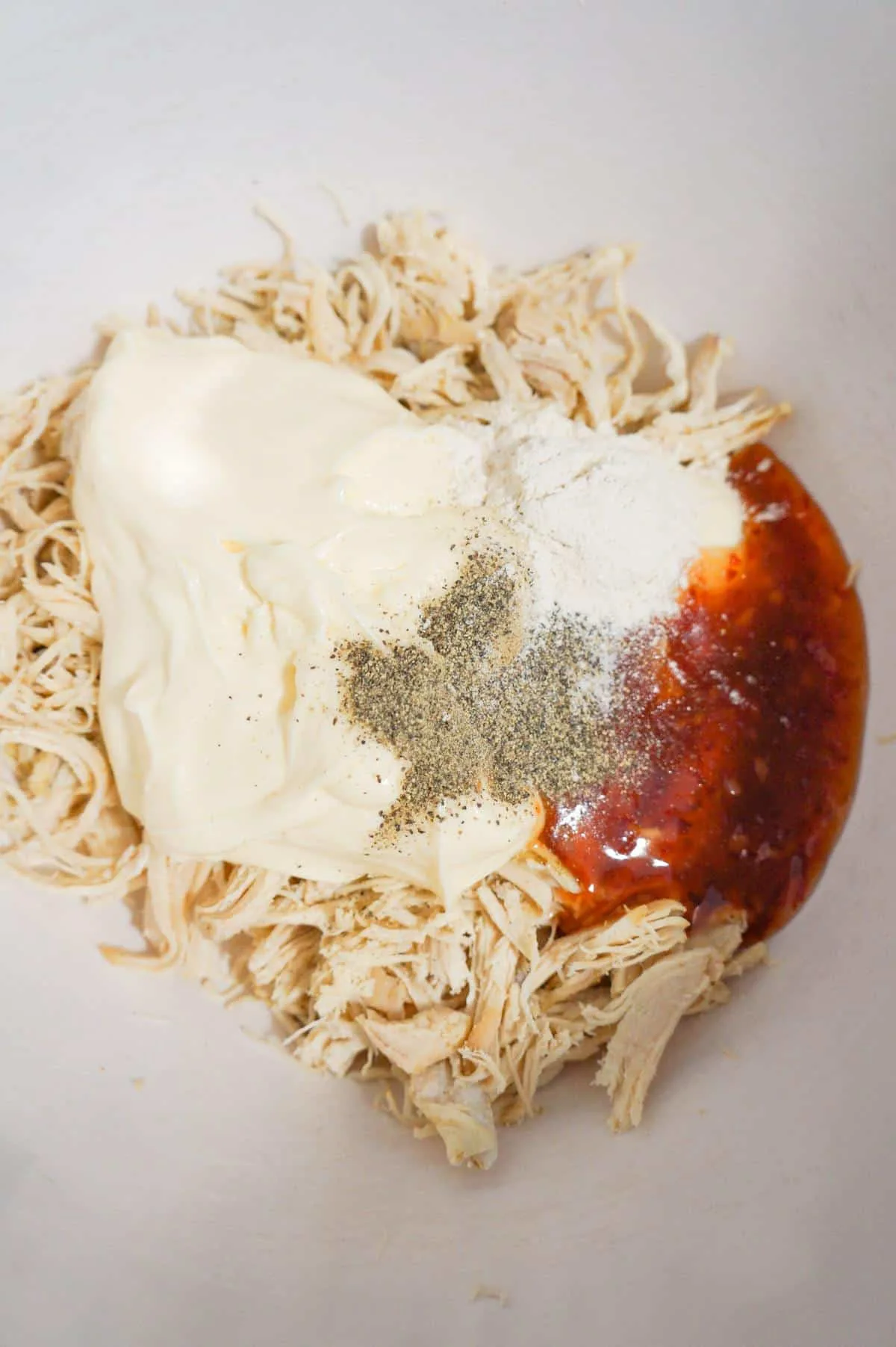 salt, pepper, mayo and sweet chili sauce on top of shredded chicken in a mixing bowl