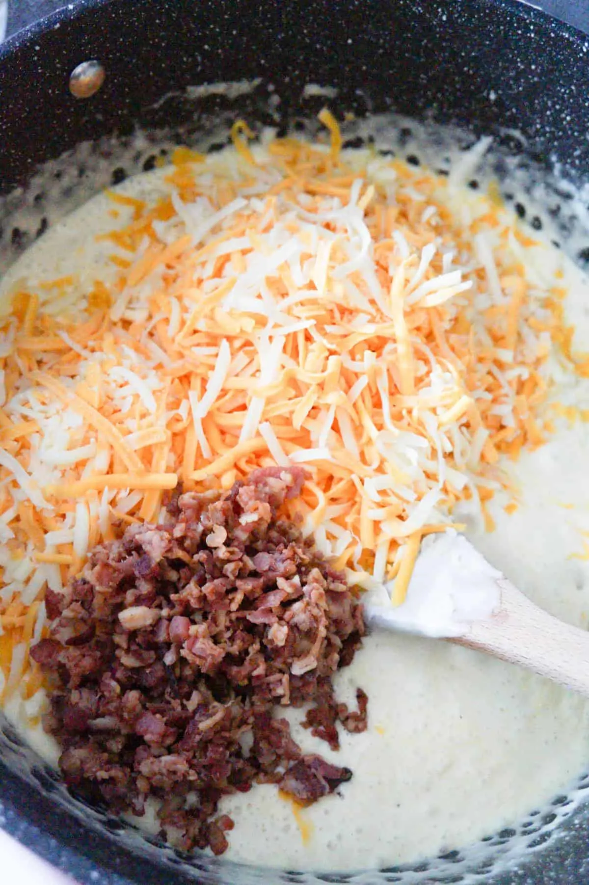 shredded mozzarella and cheddar cheese and crumbled bacon on top of creamy sauce in a large pot