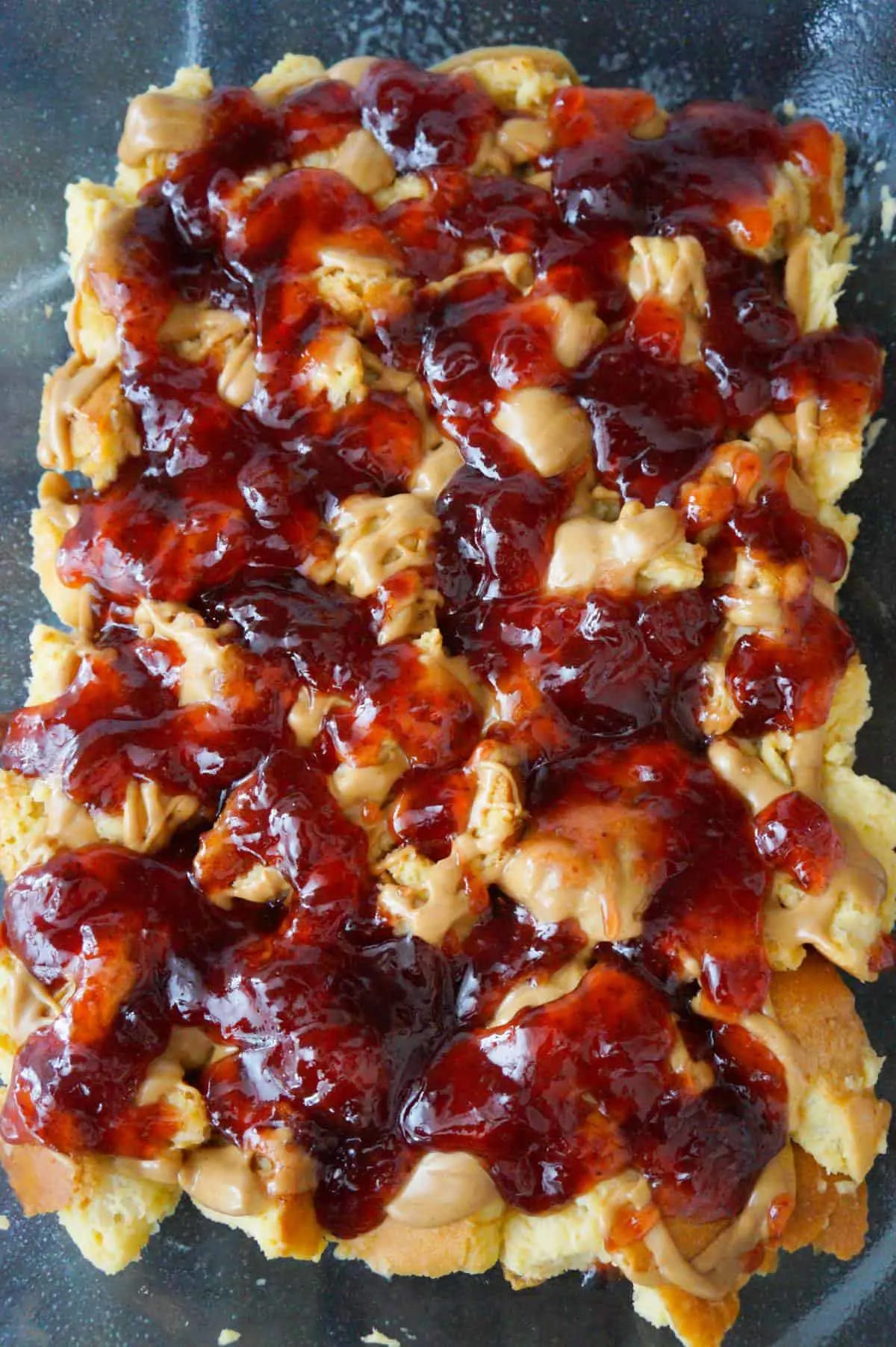 strawberry jam and peanut butter on top of cubed bread in a baking dish