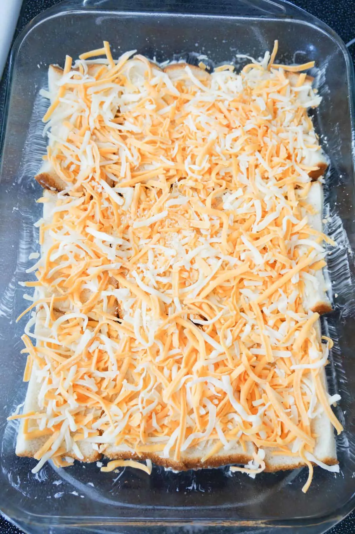 shredded mozzarella and cheddar cheese on top of bread slices in a baking dish