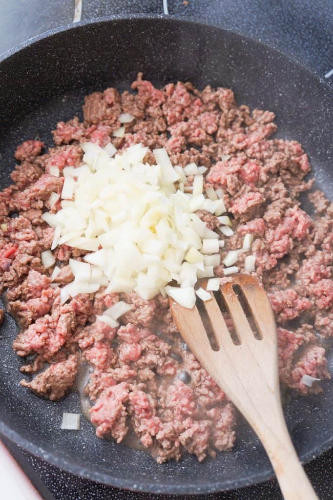 diced onions on top of ground beef in a saute pan