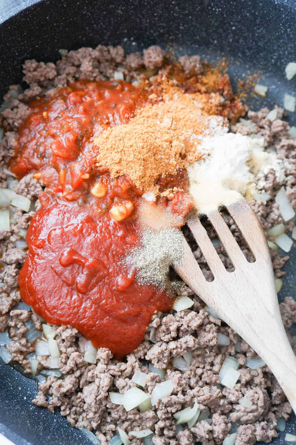 spices, salsa and chili sauce on top of cooked ground beef in a saute pan