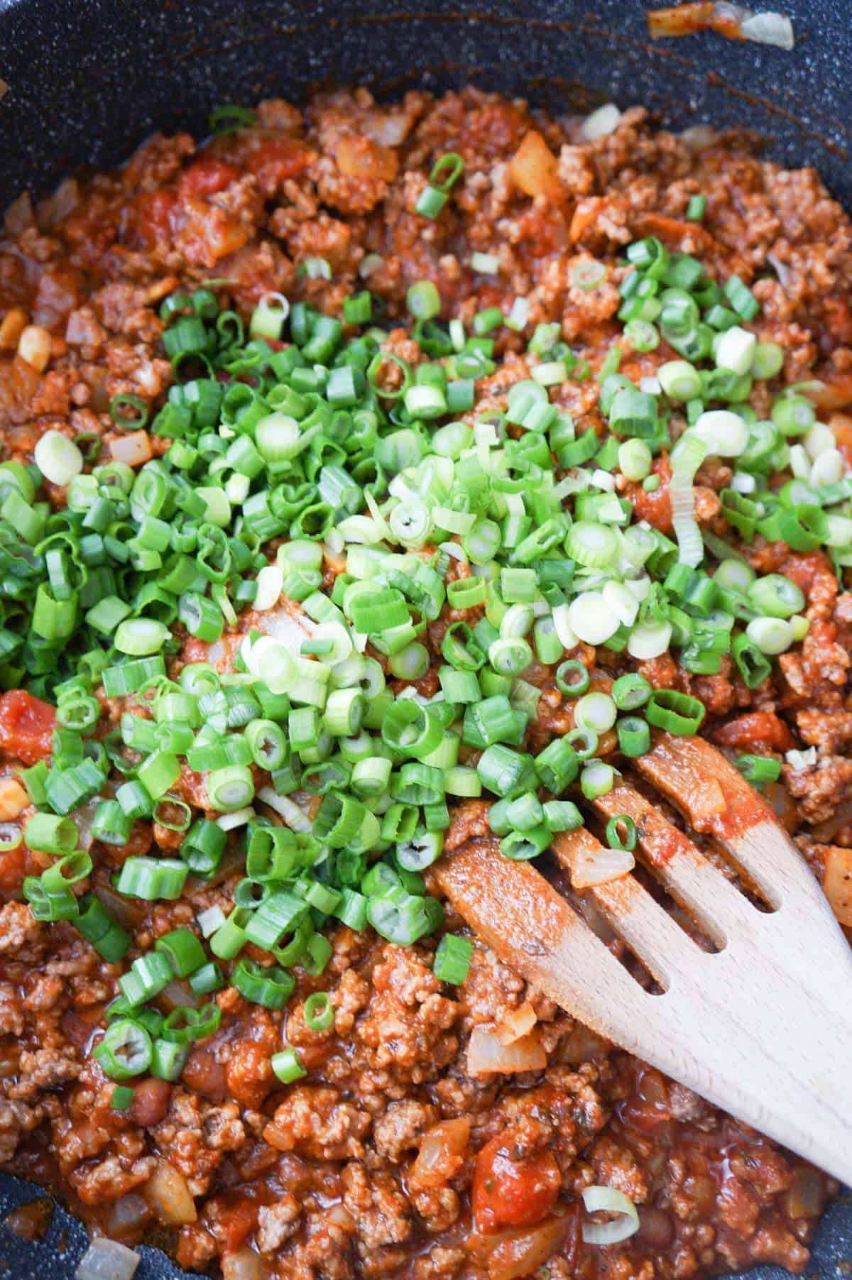 chopped green onions of on top of ground beef mixture in a saute pan