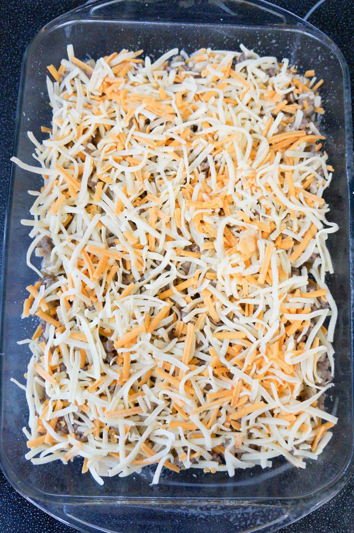 shredded cheddar cheese on top of ground beef mixture in a baking dish
