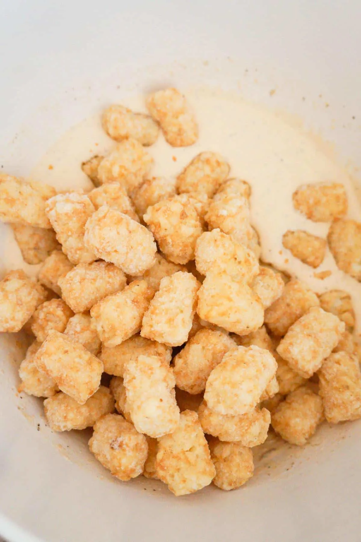 frozen tater tots in a mixing bowl with a creamy sauce