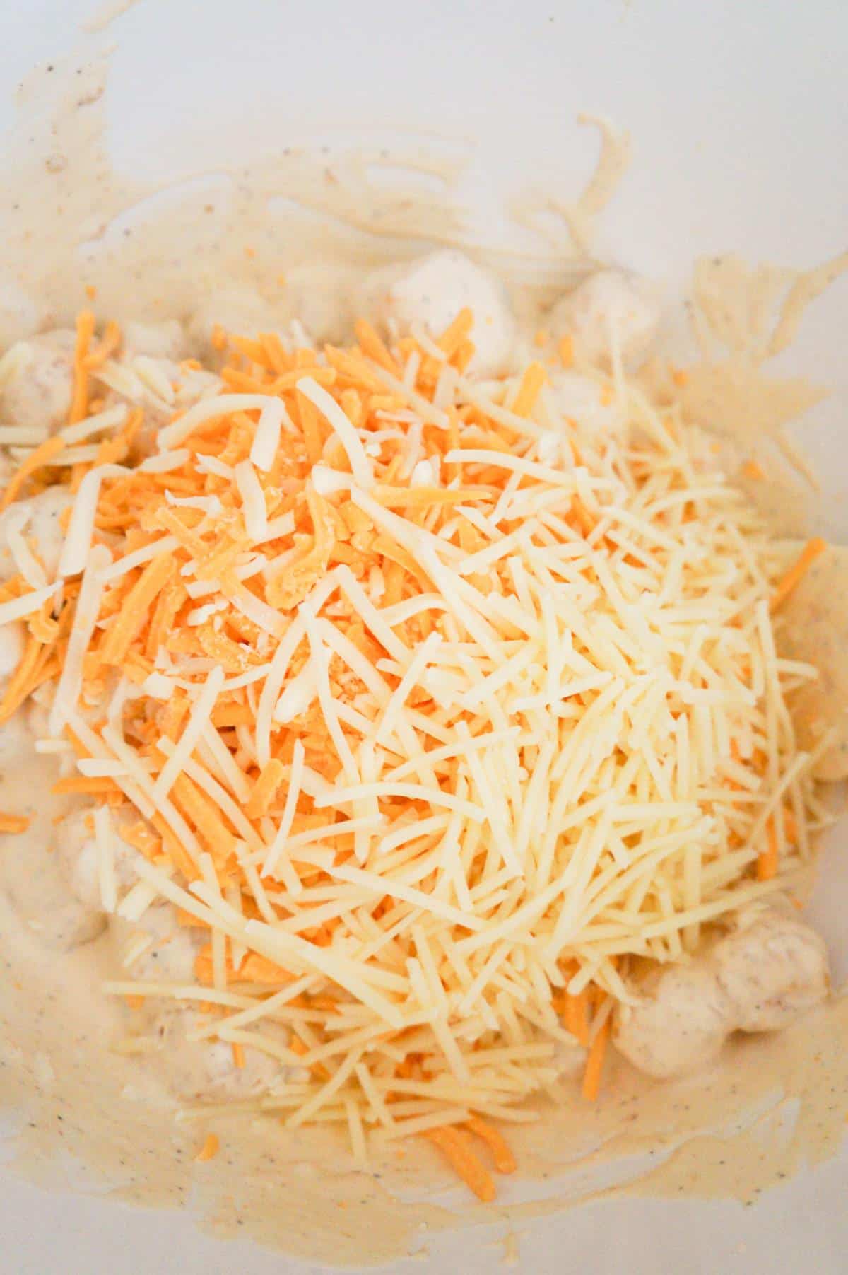 shredded parmesan, mozzarella and cheddar on top of tater tots in a mixing bowl