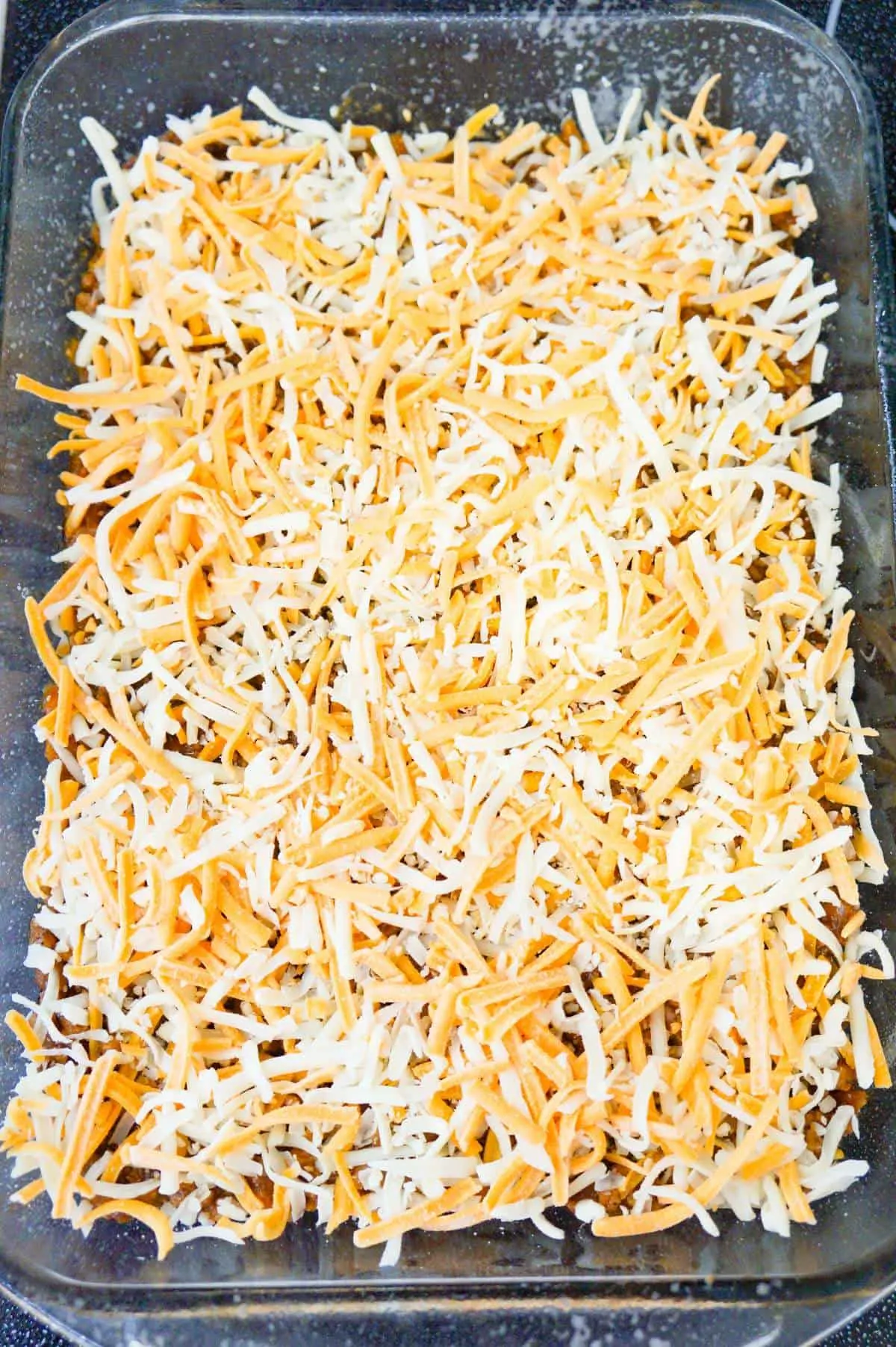 shredded cheese on top of dr pepper pork in a baking dish