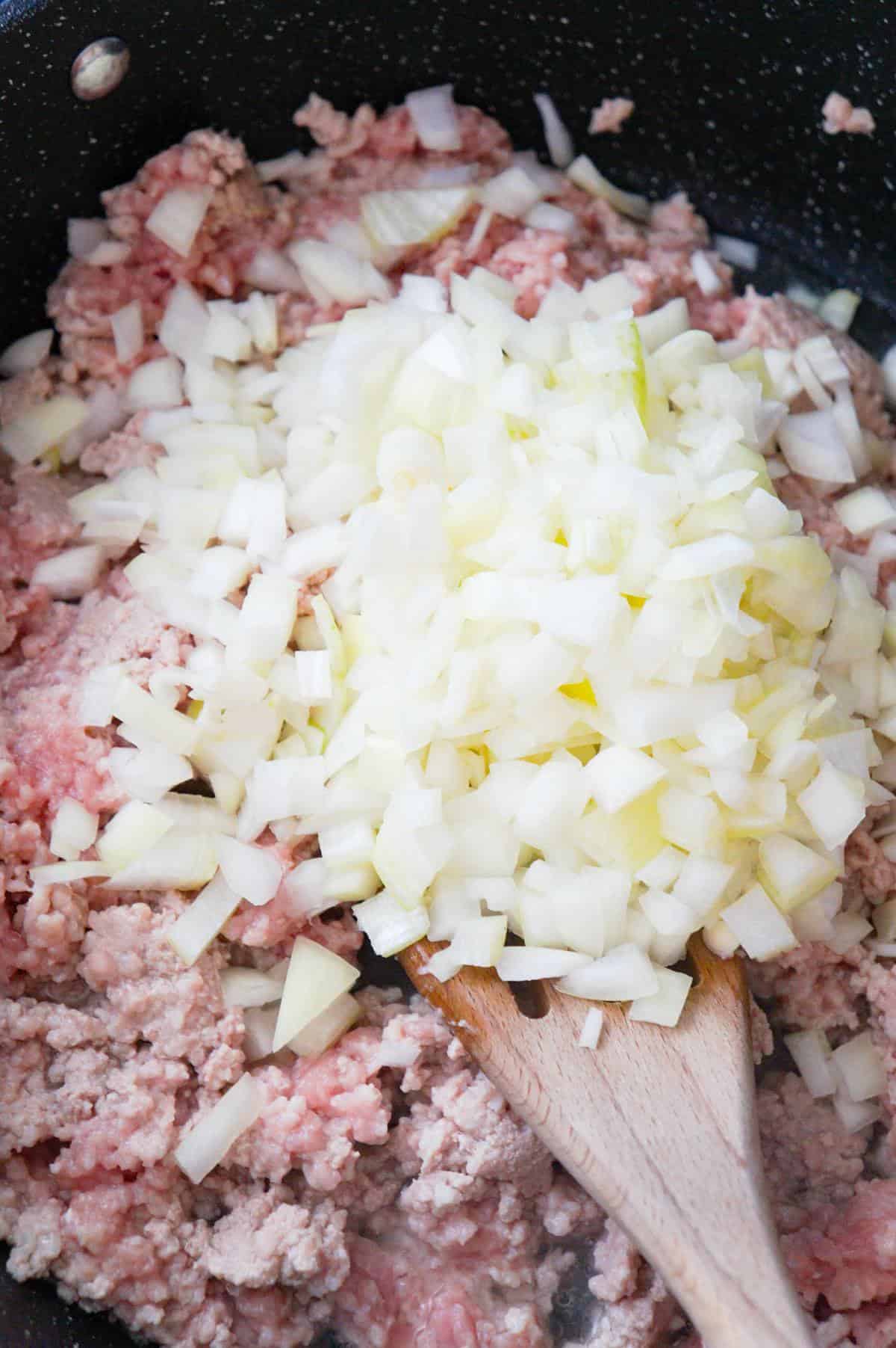 diced onions on top of ground pork in a saute pan