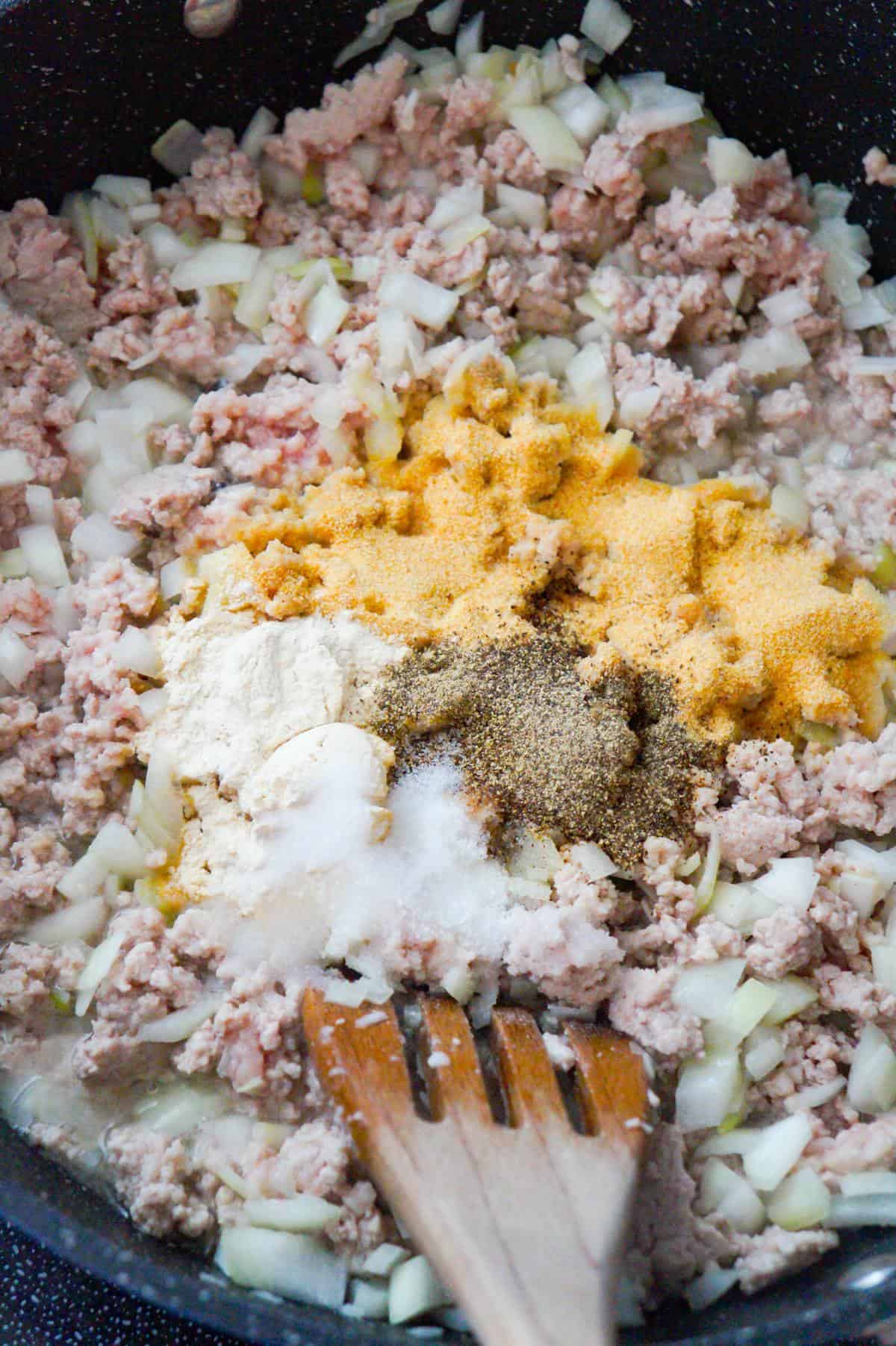 spices on top of ground pork and diced onions in a saute pan