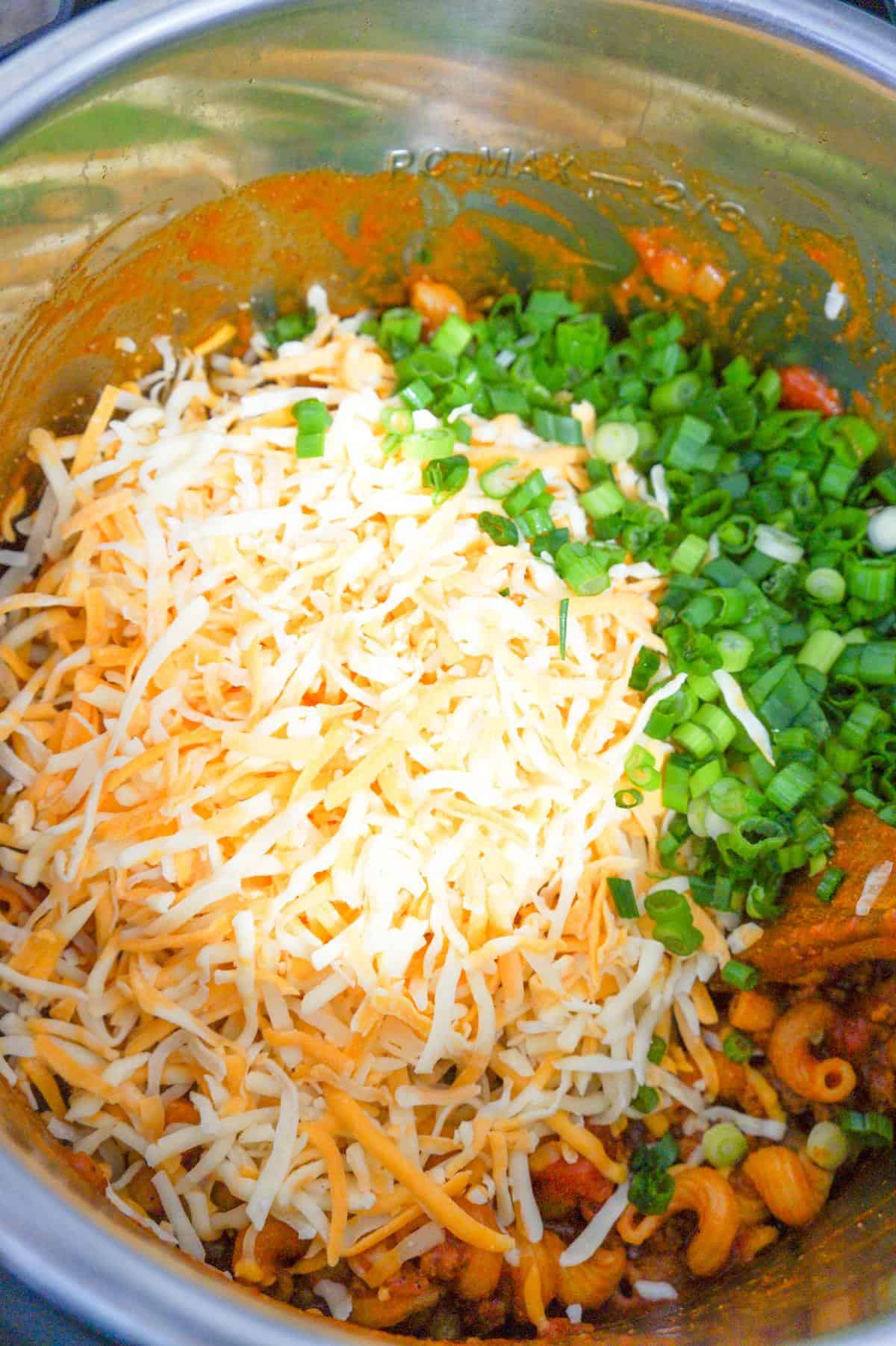 shredded cheese and chopped green onions on top of taco pasta in an Instant Pot