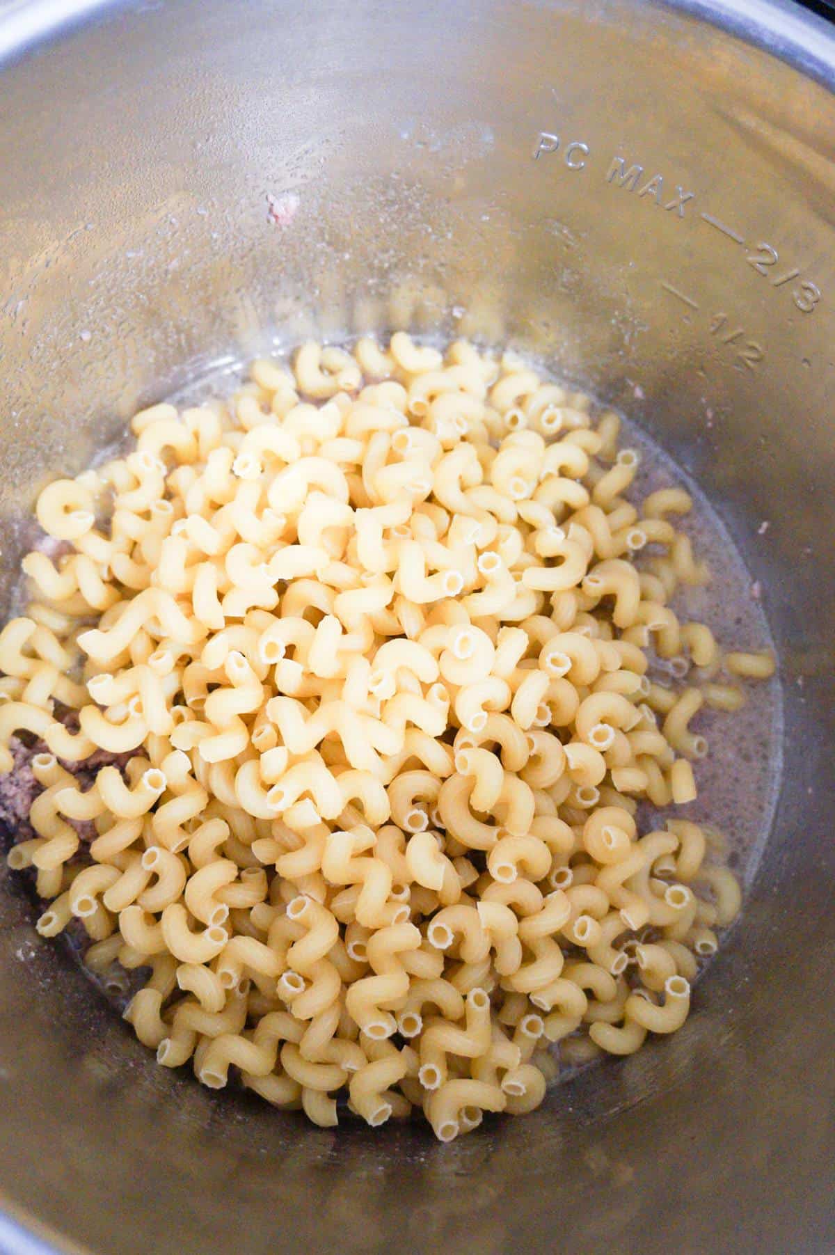 uncooked cavatappi noodles on top of water and ground beef in an Instant Pot