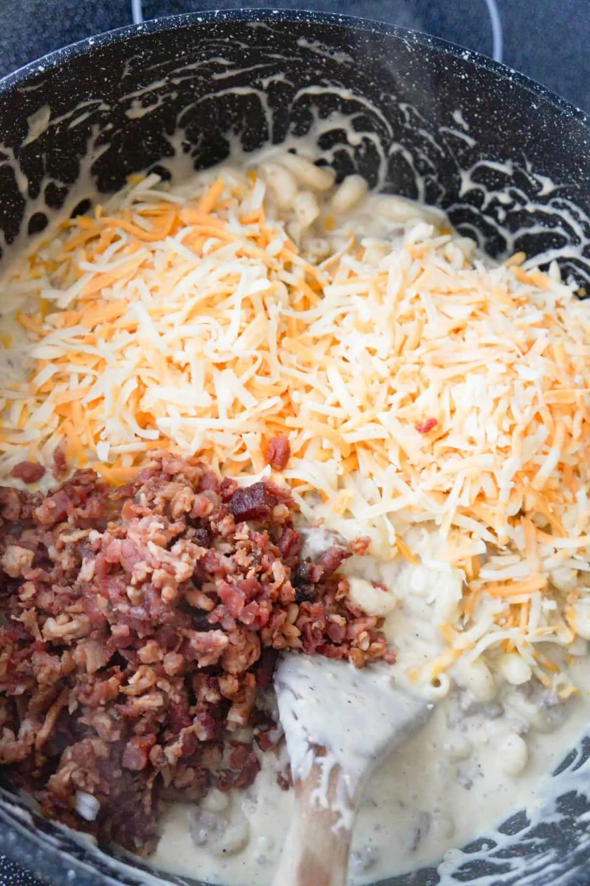 shredded cheese and crumbled bacon on top of creamy pasta in a pot