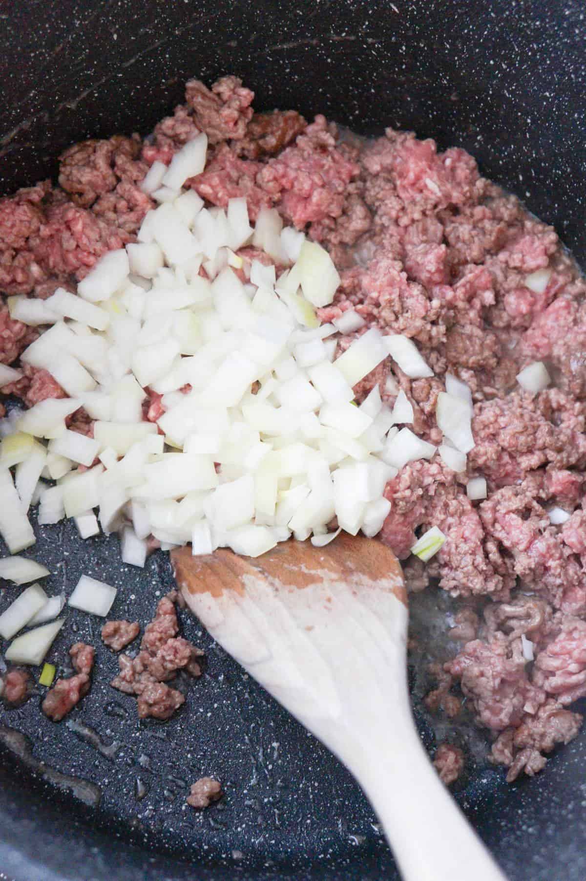 diced onions on top of ground beef cooking in a pot