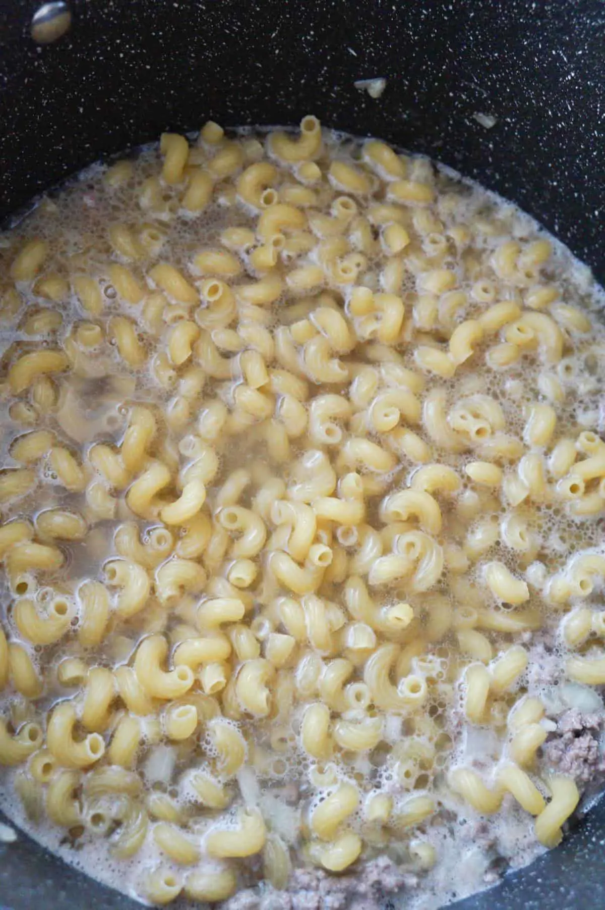 cavatappi noodles, water and ground beef in a pot