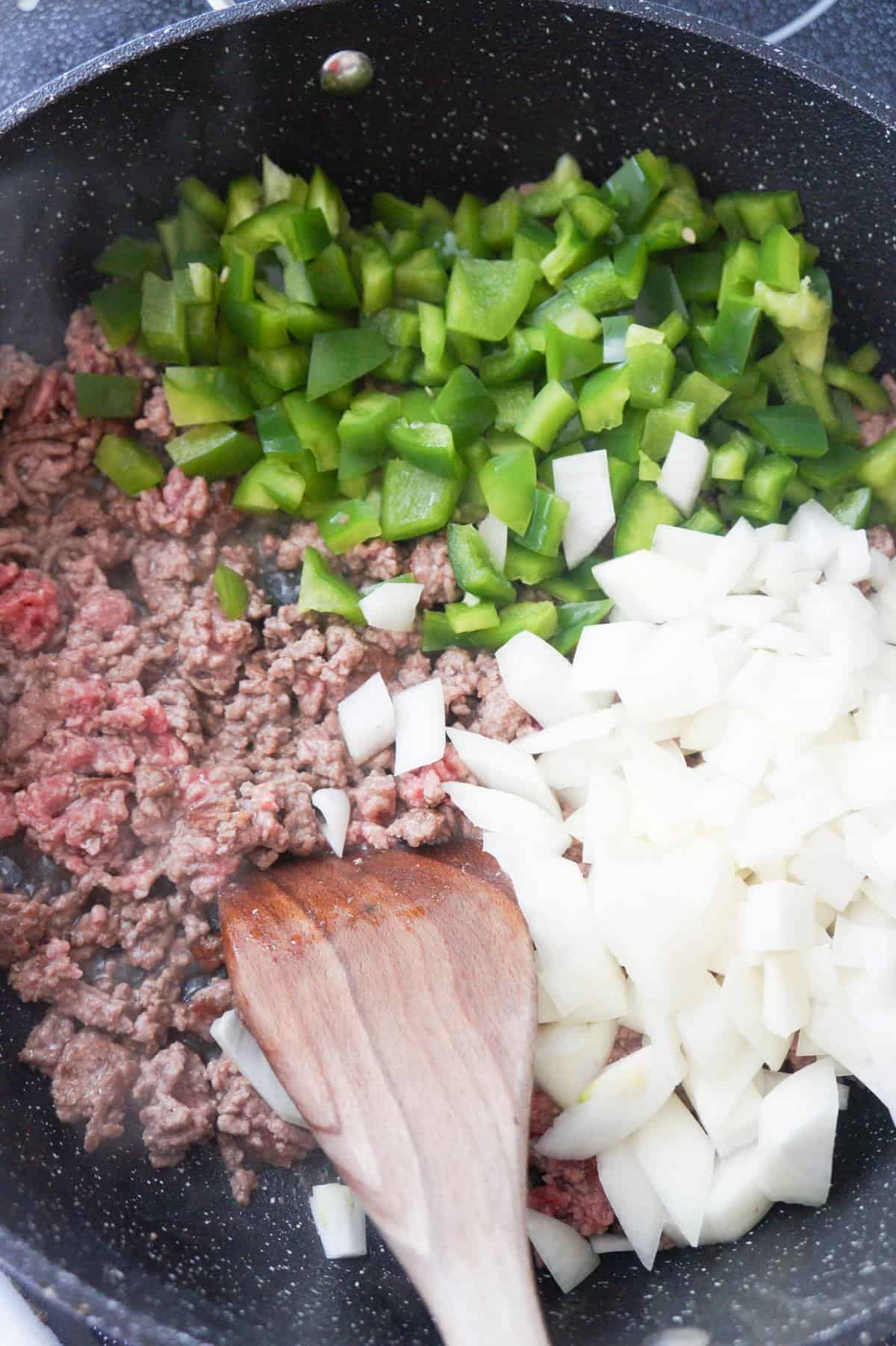 diced green peppers and diced onions on top of ground beef in a saute pan