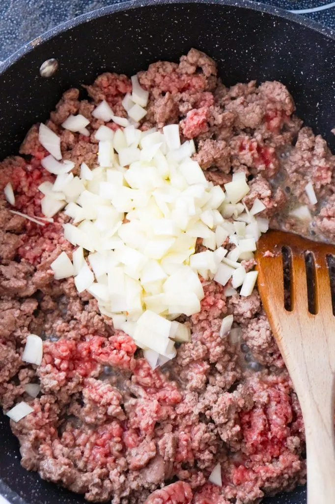 diced onions on top of ground beef in a saute pan