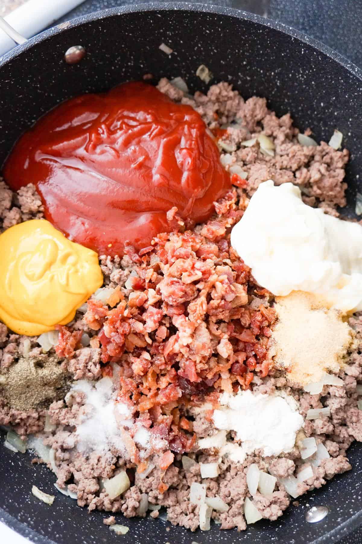 crumbled bacon, ketchup, mustard and mayo on top of ground beef in a saute pan