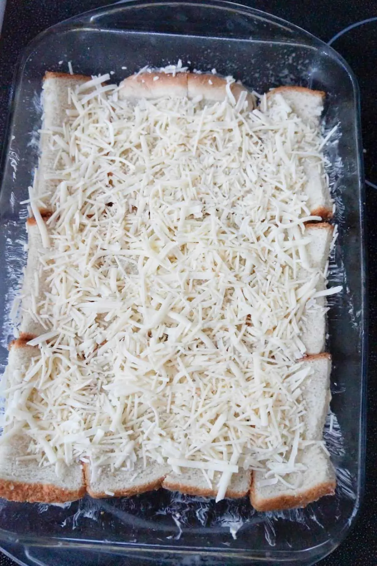 shredded cheese on top of bread in a baking dish
