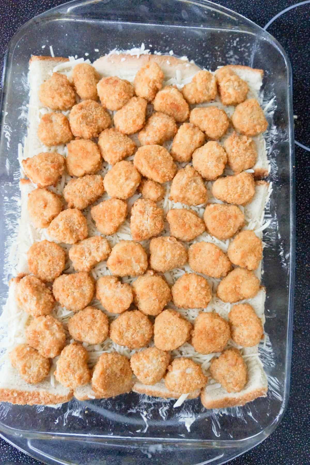 popcorn chicken and shredded cheese on top of bread in a baking dish