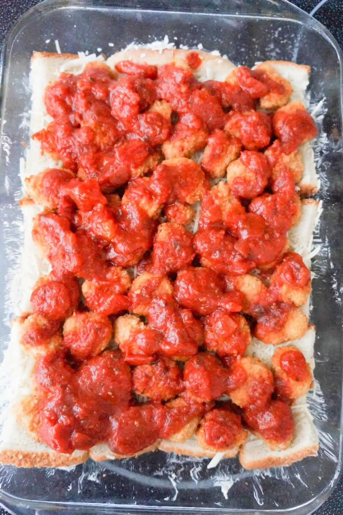 marinara sauce on top of popcorn chicken and bread in a baking dish
