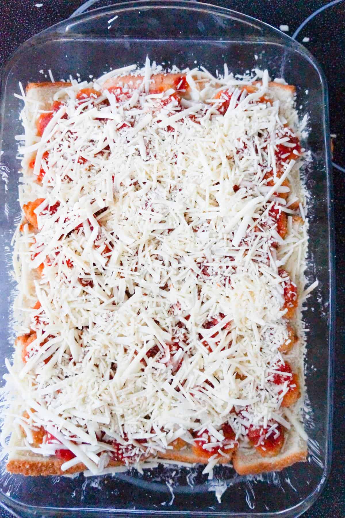 shredded cheese on top of popcorn chicken in a baking dish