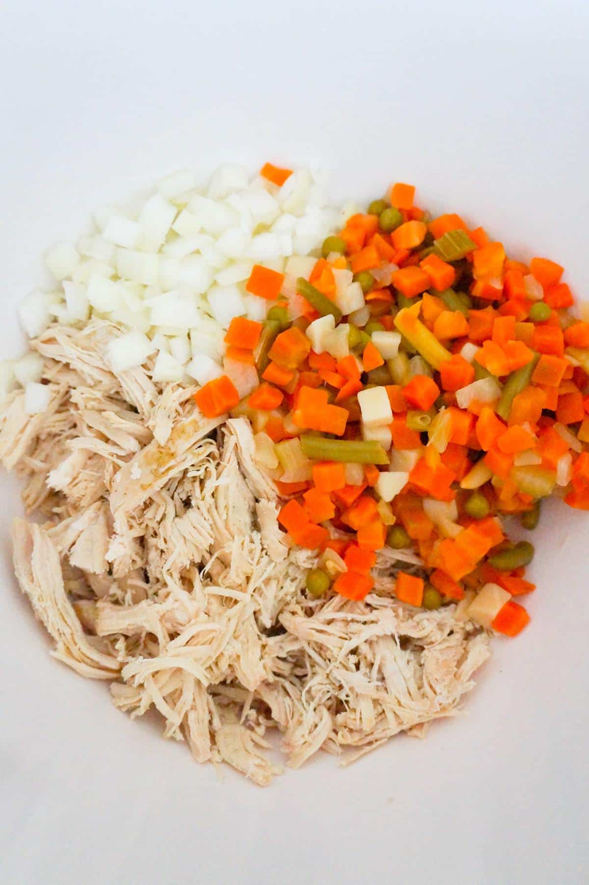shredded chicken, diced onions and mixed veggies in a mixing bowl