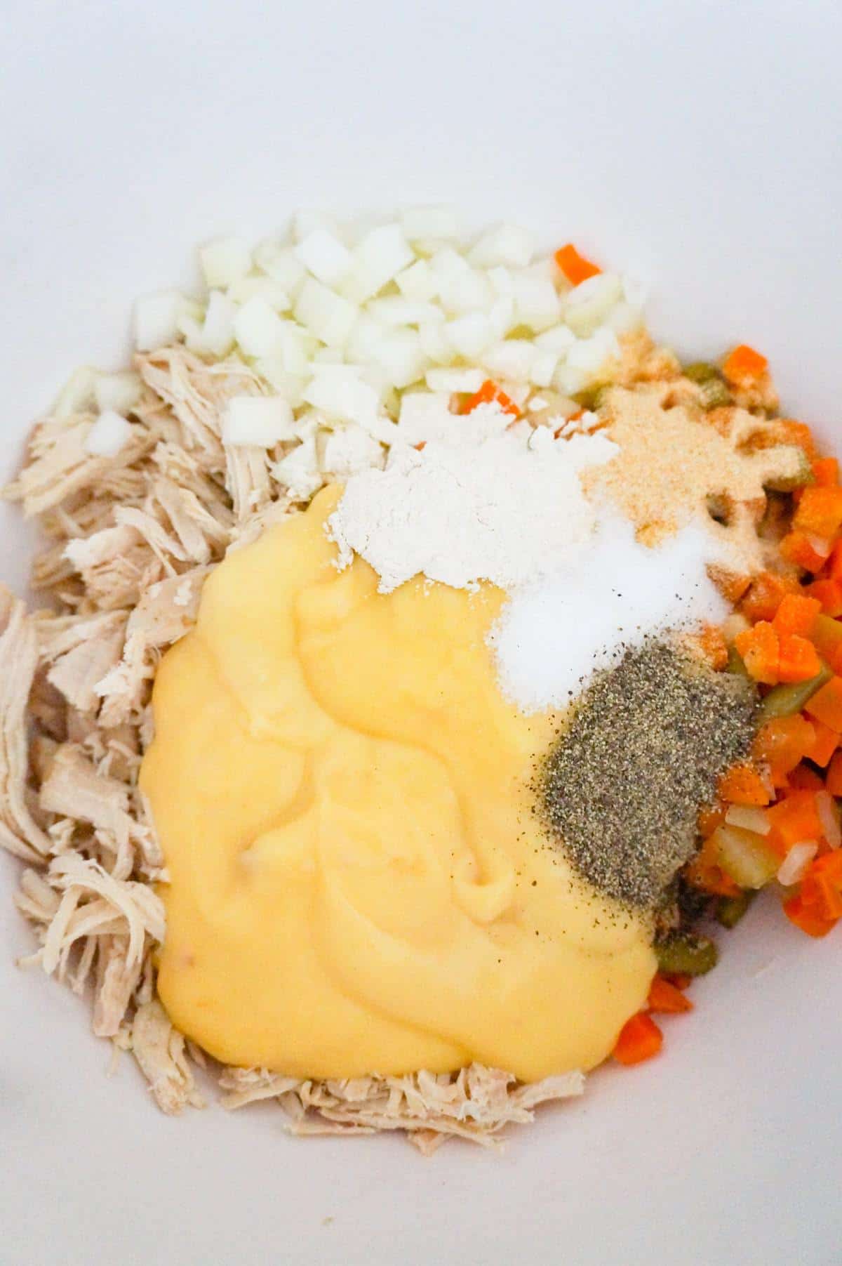 cream of chicken soup and spices on top of shredded chicken and veggies in a mixing bowl