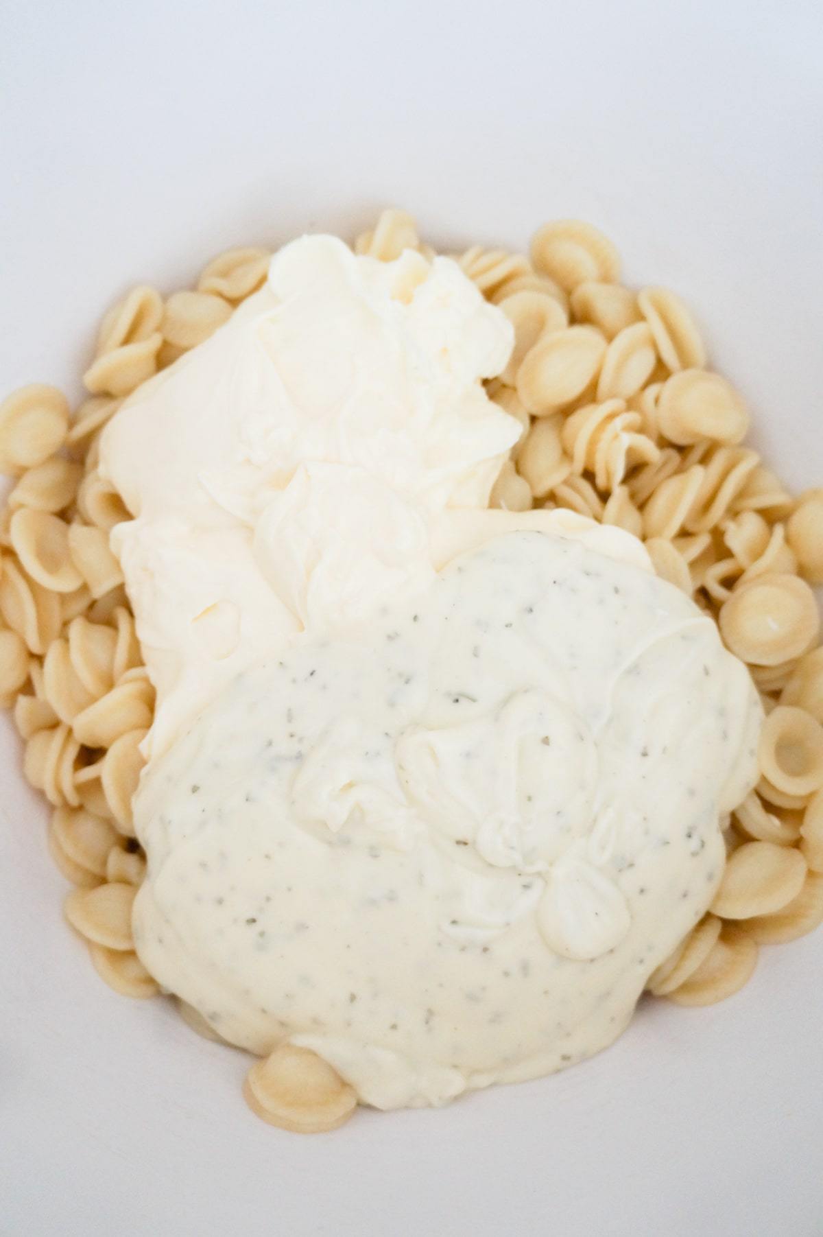 mayo and ranch dressing on top of pasta in a mixing bowl