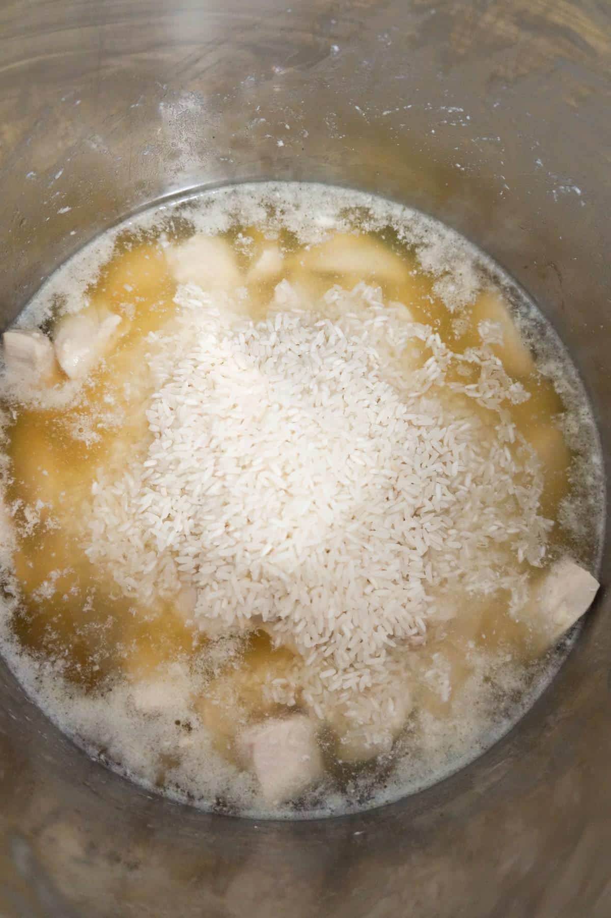 long grain white rice on top of chicken in broth in an Instant Pot
