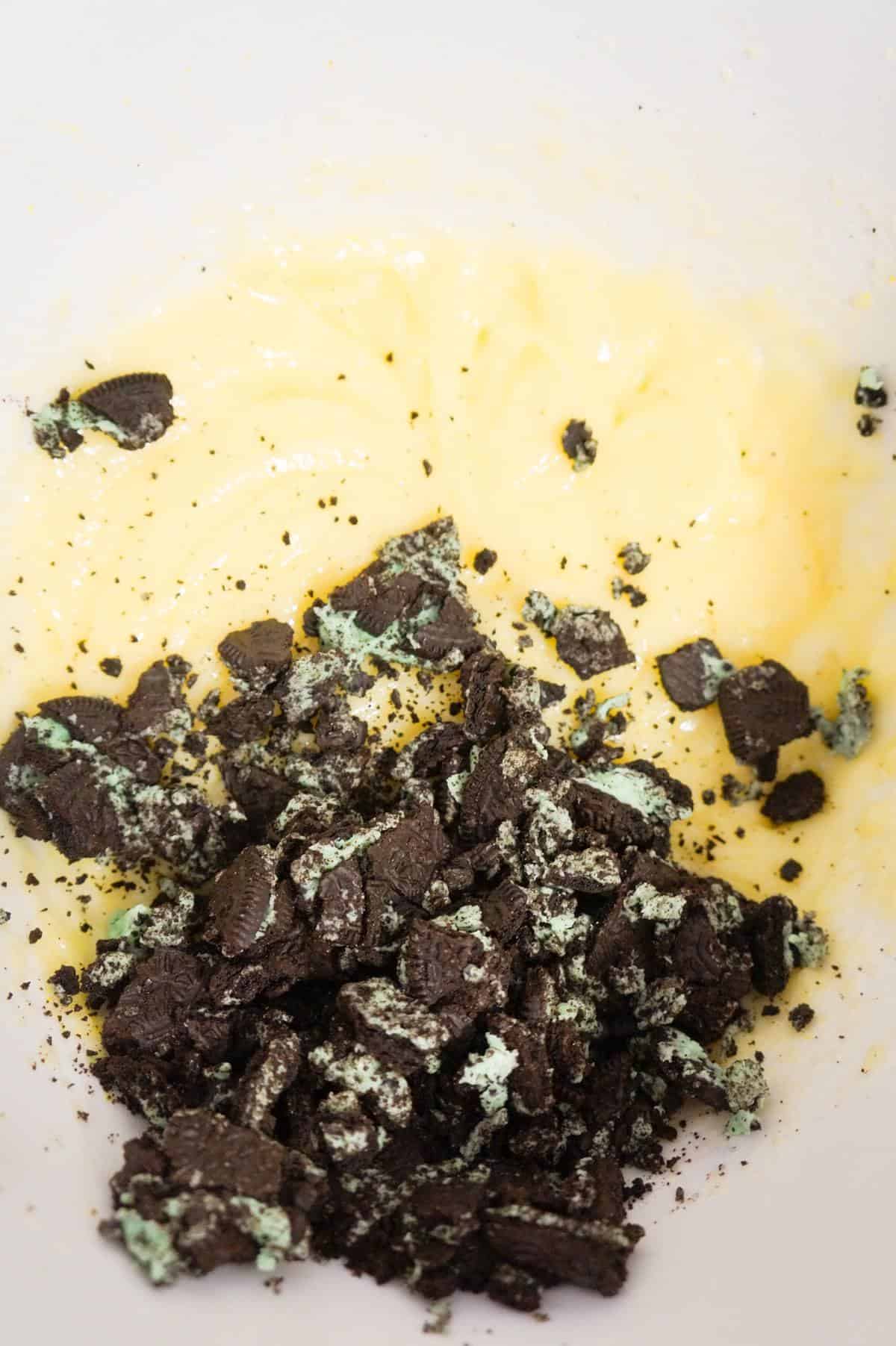crumbled mint oreo cookies on top of vanilla pudding mixture in a mixing bowl