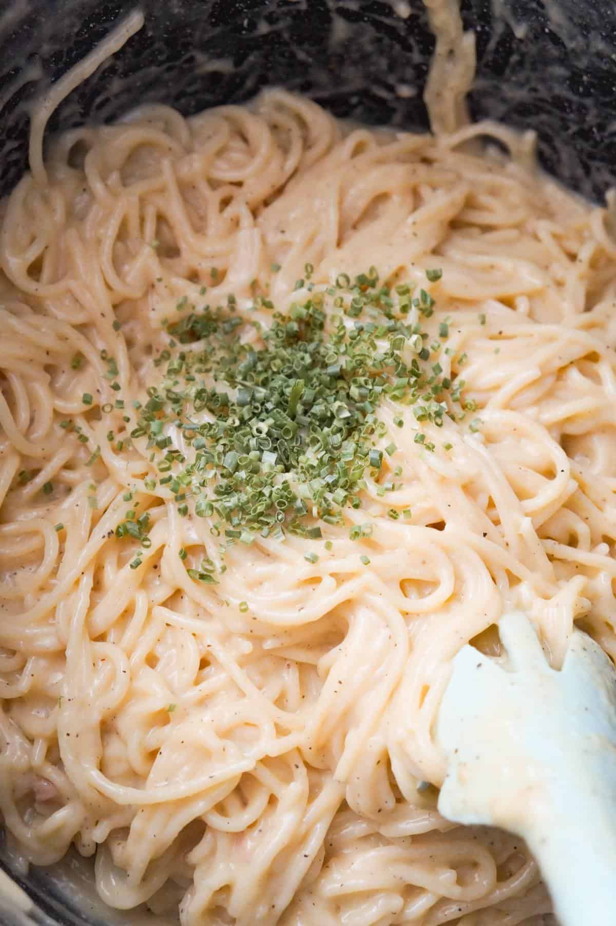 chopped chives on top of creamy spaghetti in a pot