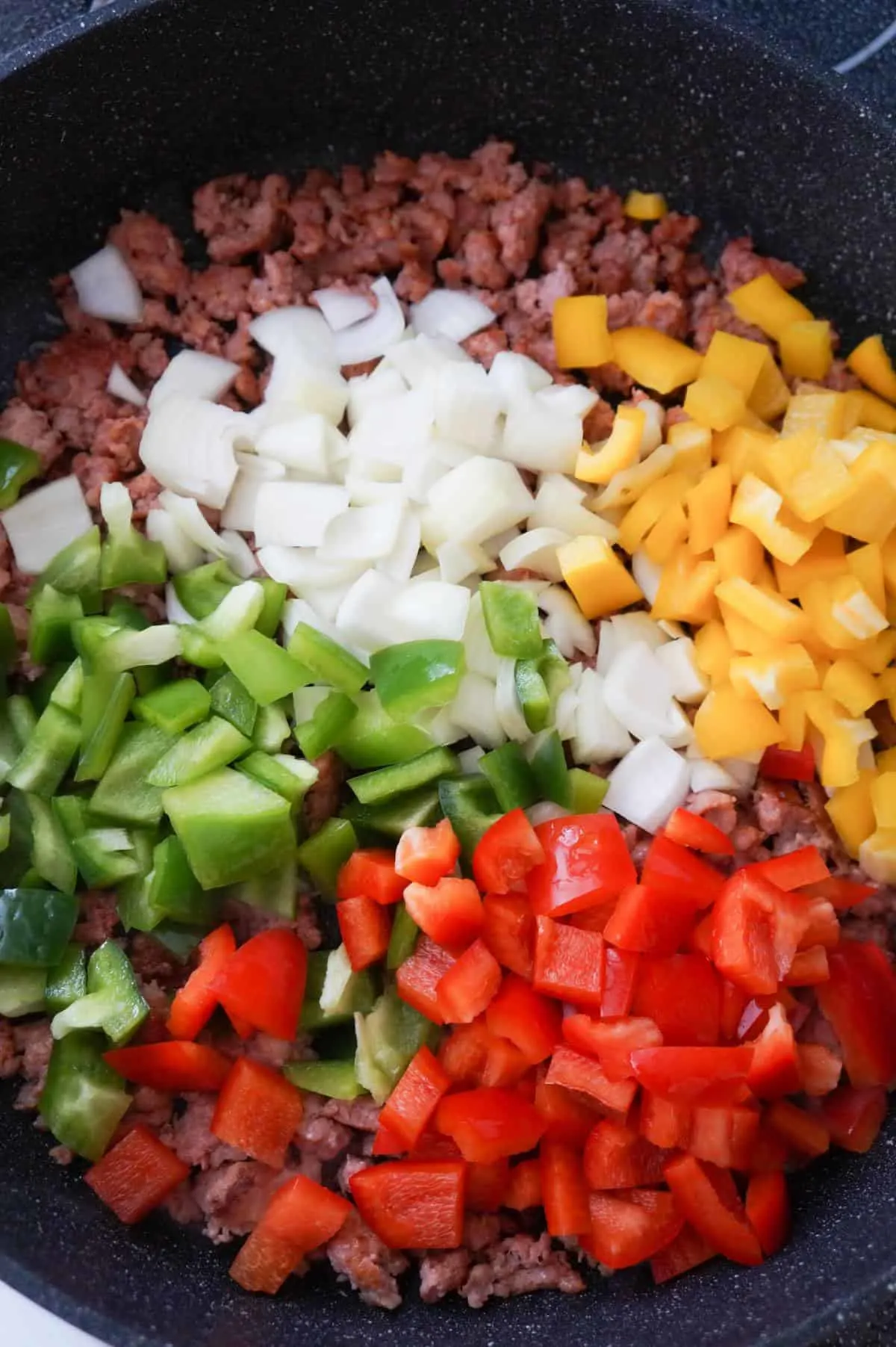 diced onion and diced peppers on top of ground sausage meat in a saute pan