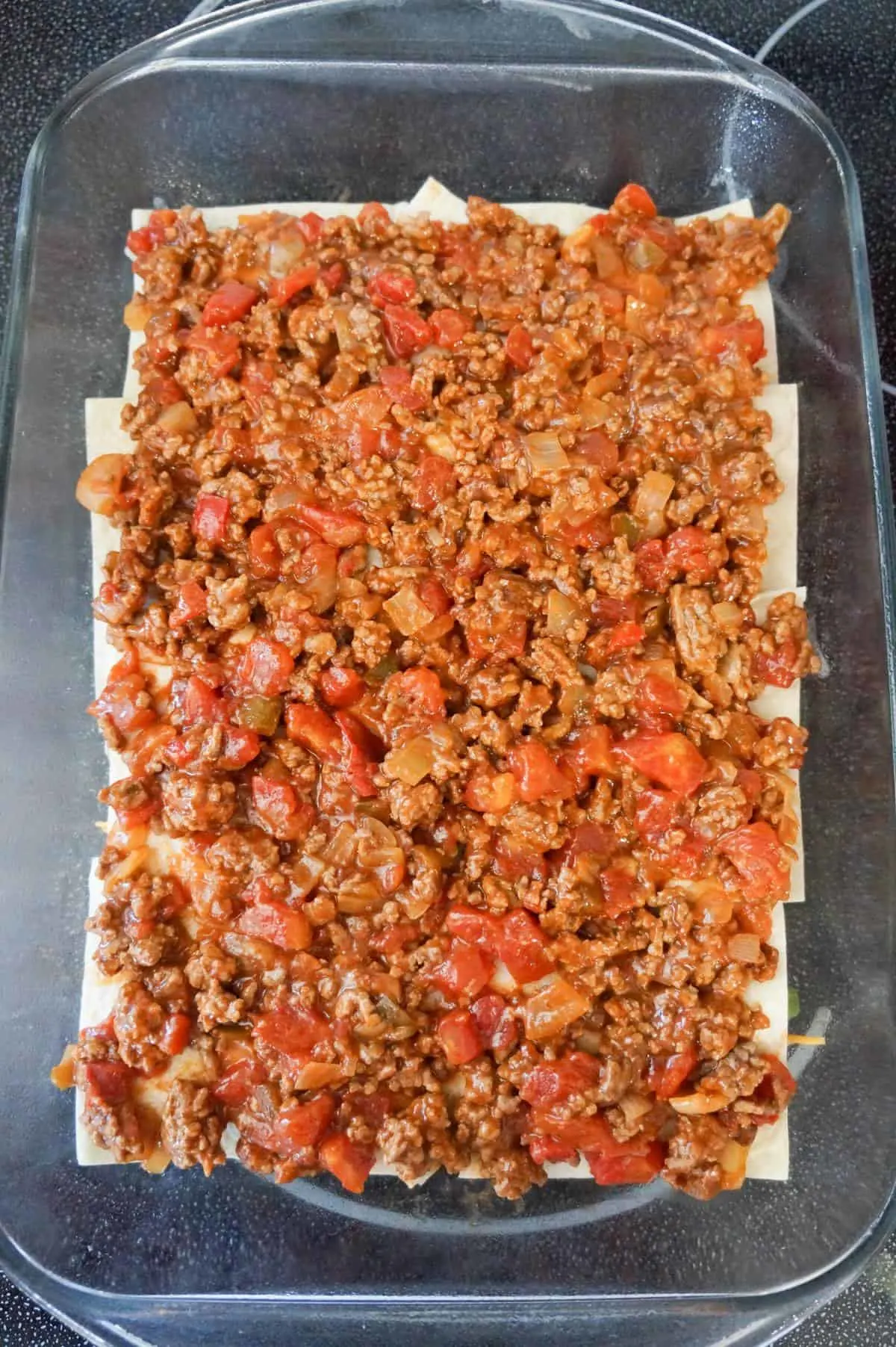 ground beef and salsa mixture on top of flour tortilla pieces in a baking dish