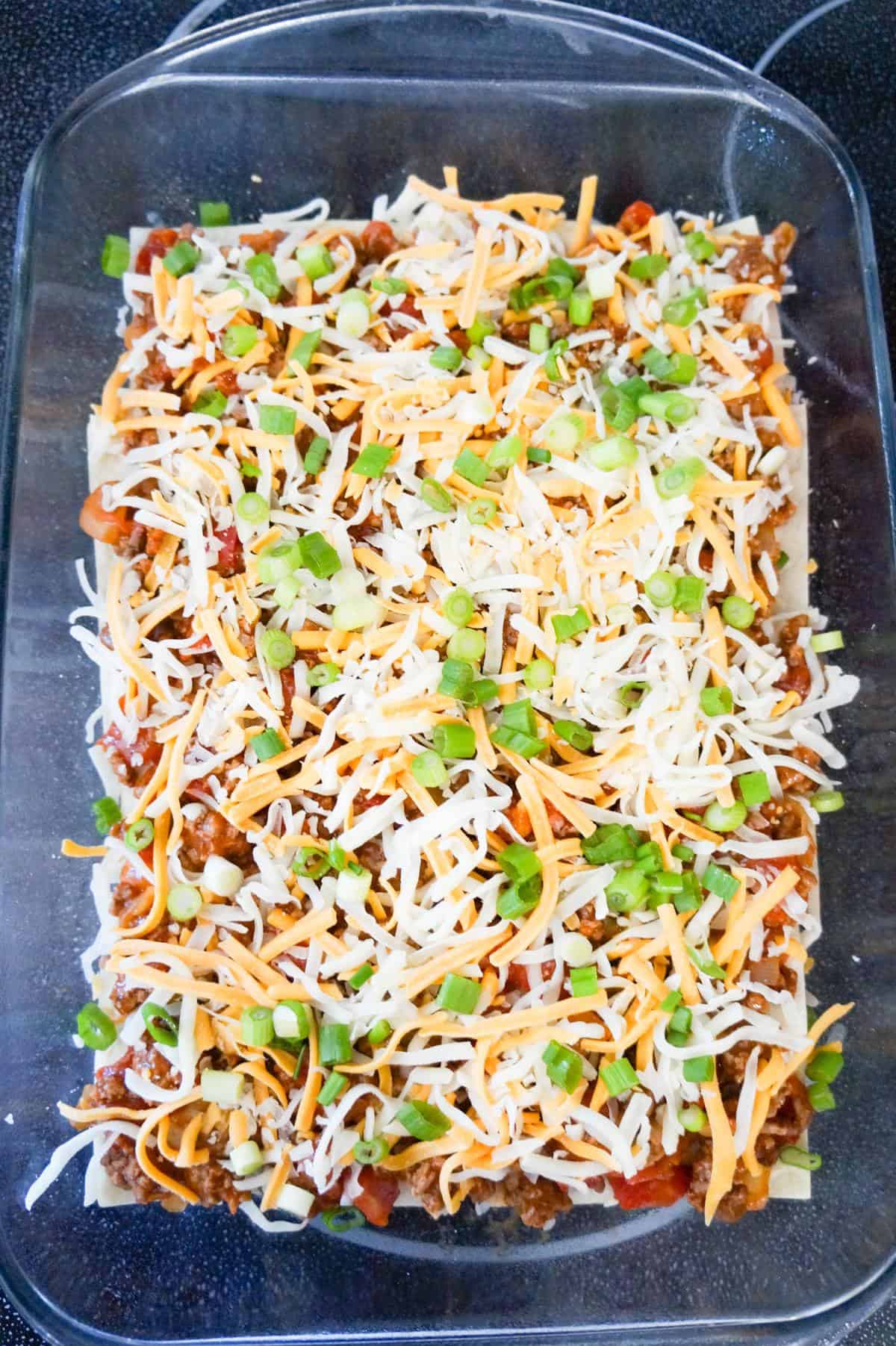 chopped green onions and shredded cheese on top of meat mixture in a baking dish