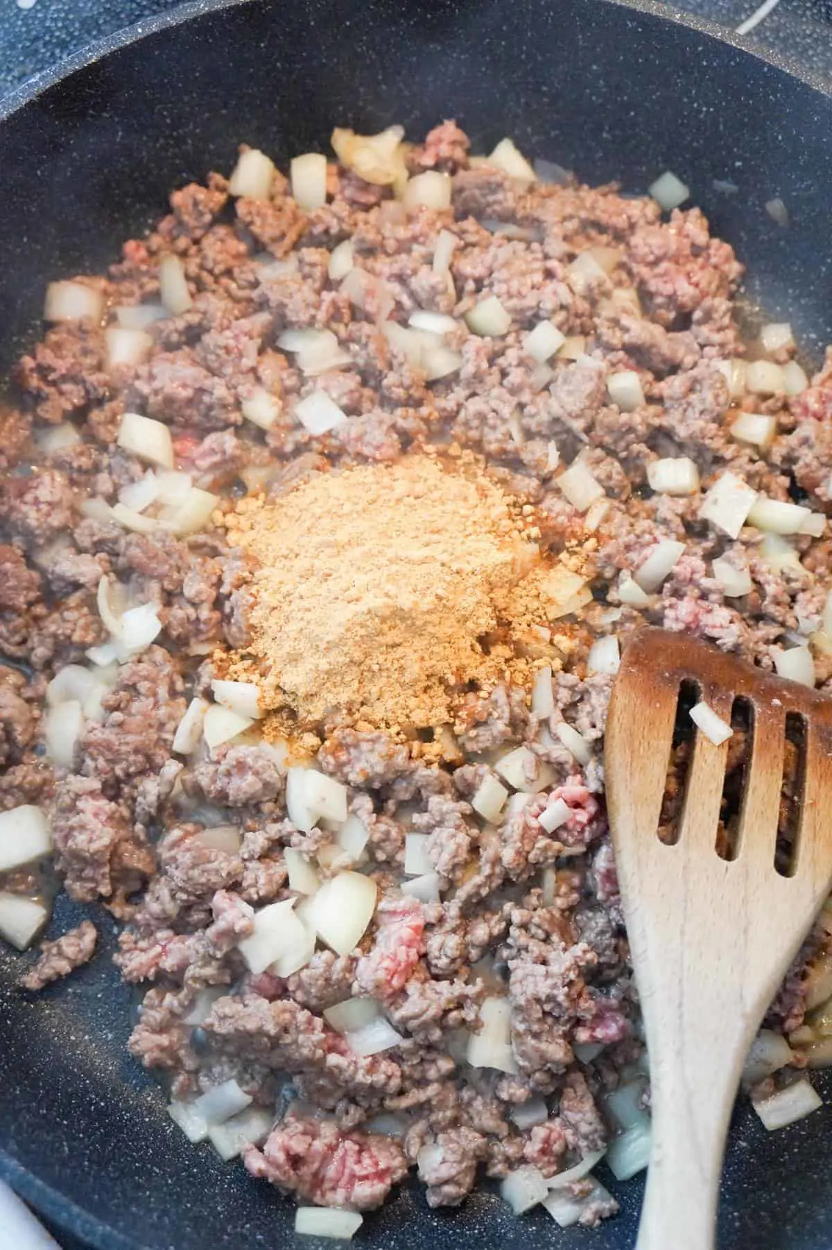 taco seasoning on top of ground beef and diced onions in a saute pan