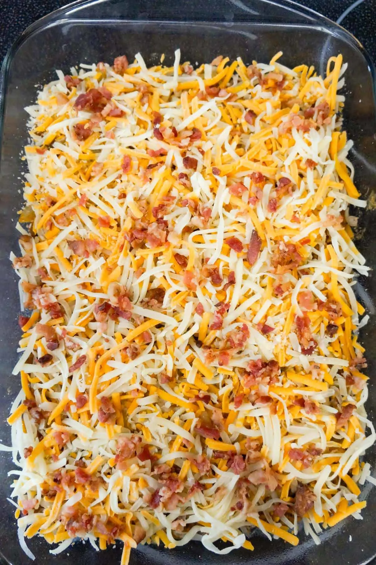 crumbled bacon and shredded cheese on top of cheeseburger casserole before baking