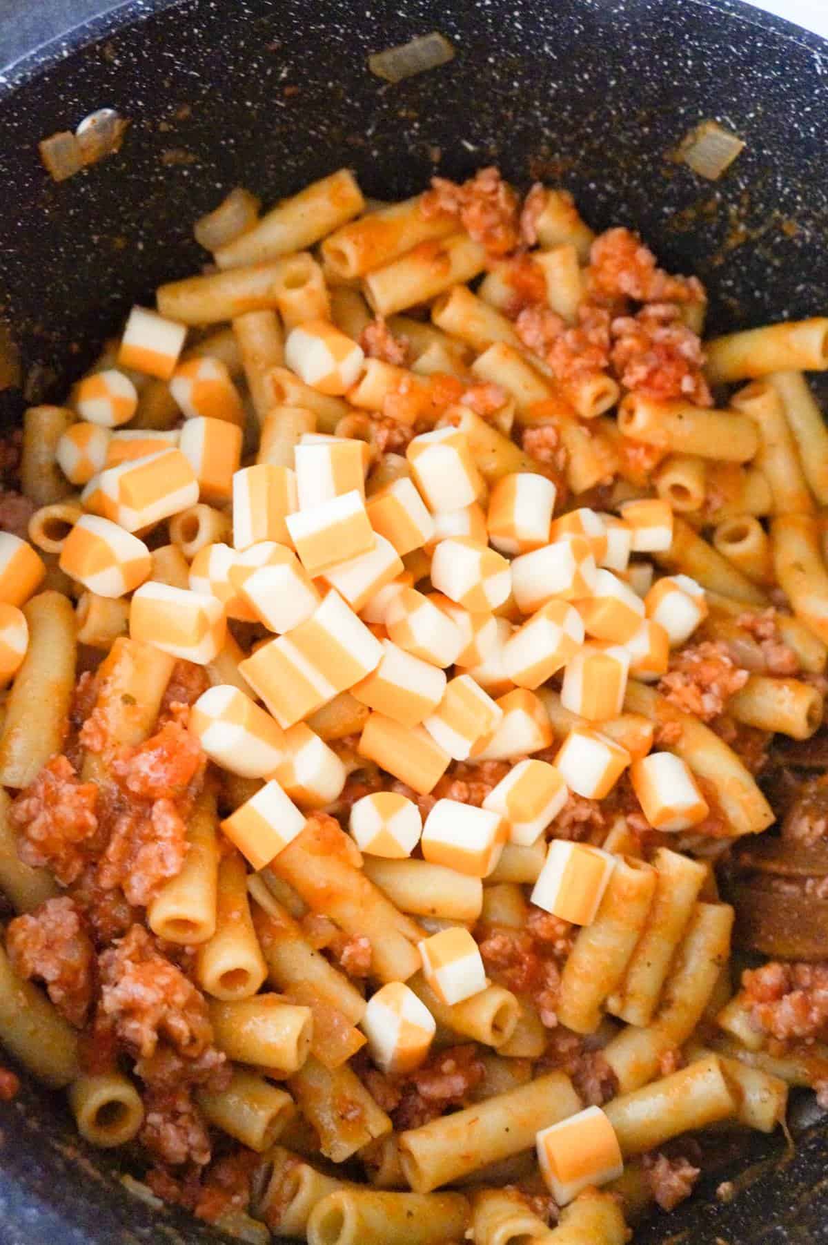 cubes of string cheese on top of sausage ziti in a large pot