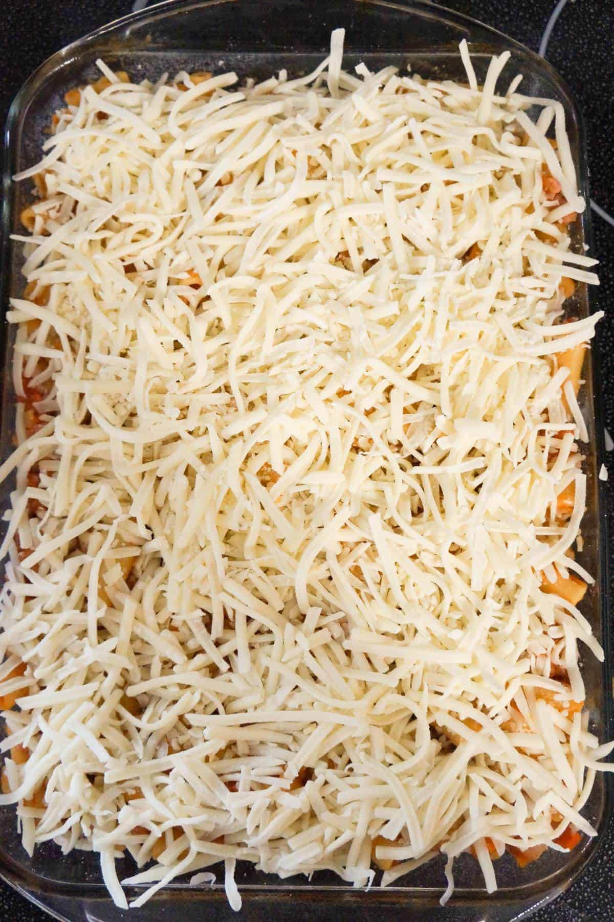 shredded mozzarella cheese on top of sausage ziti in a baking dish